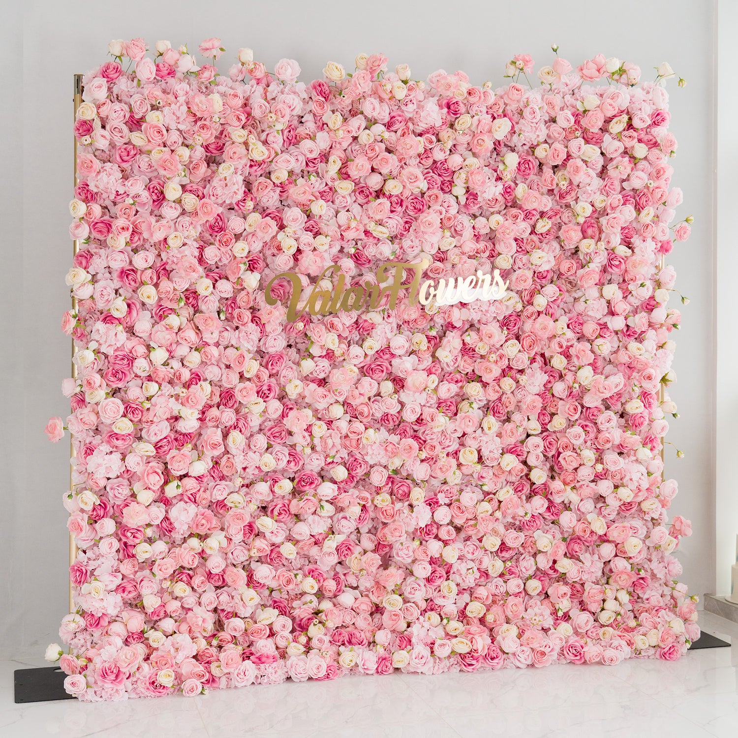 This photo showcases a large floral backdrop densely filled with roses in soft pink and white hues. The lush arrangement creates a dreamy, romantic atmosphere. Prominently displayed in the center is the “ValarFlowers” logo in elegant gold lettering. Ideal for weddings, bridal showers, or other romantic events, this backdrop exudes charm and sophistication, making it a stunning decorative piece.