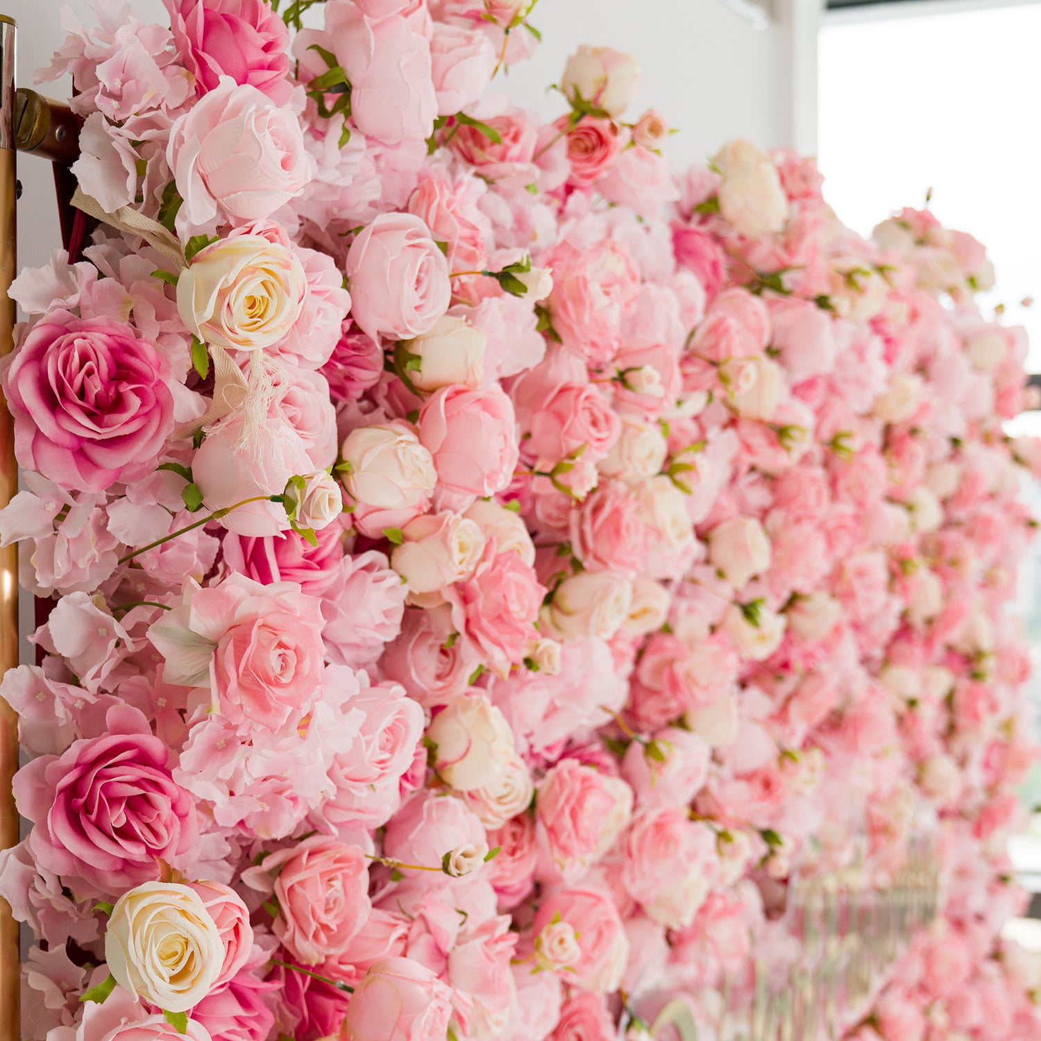 This photo showcases a lush, vibrant floral arrangement. It is densely packed with an array of roses in soft pink and white hues, creating a dreamy and romantic atmosphere. The delicate petals and green foliage are meticulously arranged, likely serving as a backdrop for events such as weddings or bridal showers. The overall effect is one of elegance and charm, making it a striking decorative element.