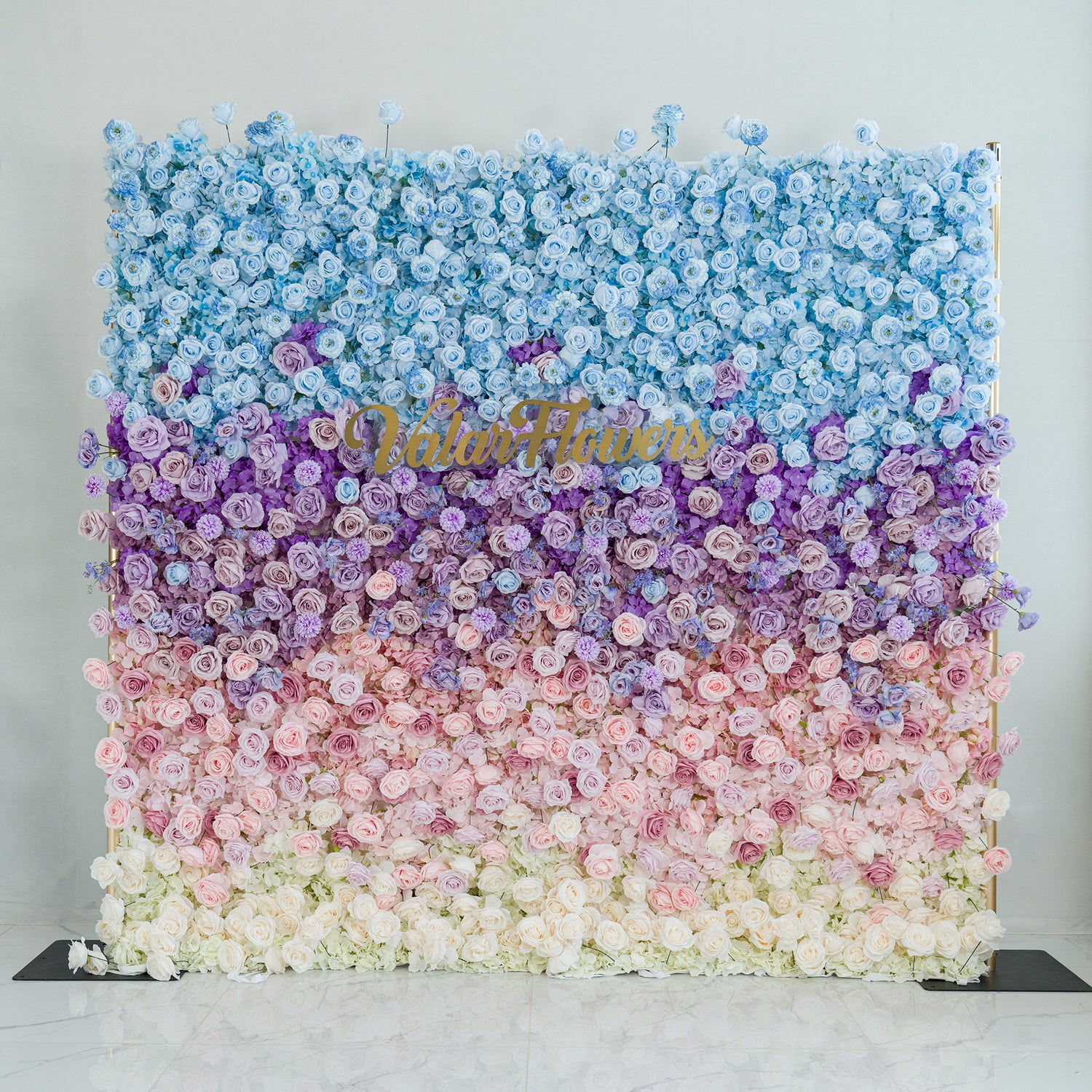 This grand floral wall showcases a gradient of roses, with blooms in blue, purple, pink, and white. The ombre color theme, transitioning smoothly from deep blues to soft whites, creates a dreamy, elegant vibe. Perfect for weddings, galas, or brand activations, the gold “ValarFlowers” sign adds sophistication. It’s a standout photo - worthy backdrop, blending natural beauty with polished design, ideal for memorable event moments.