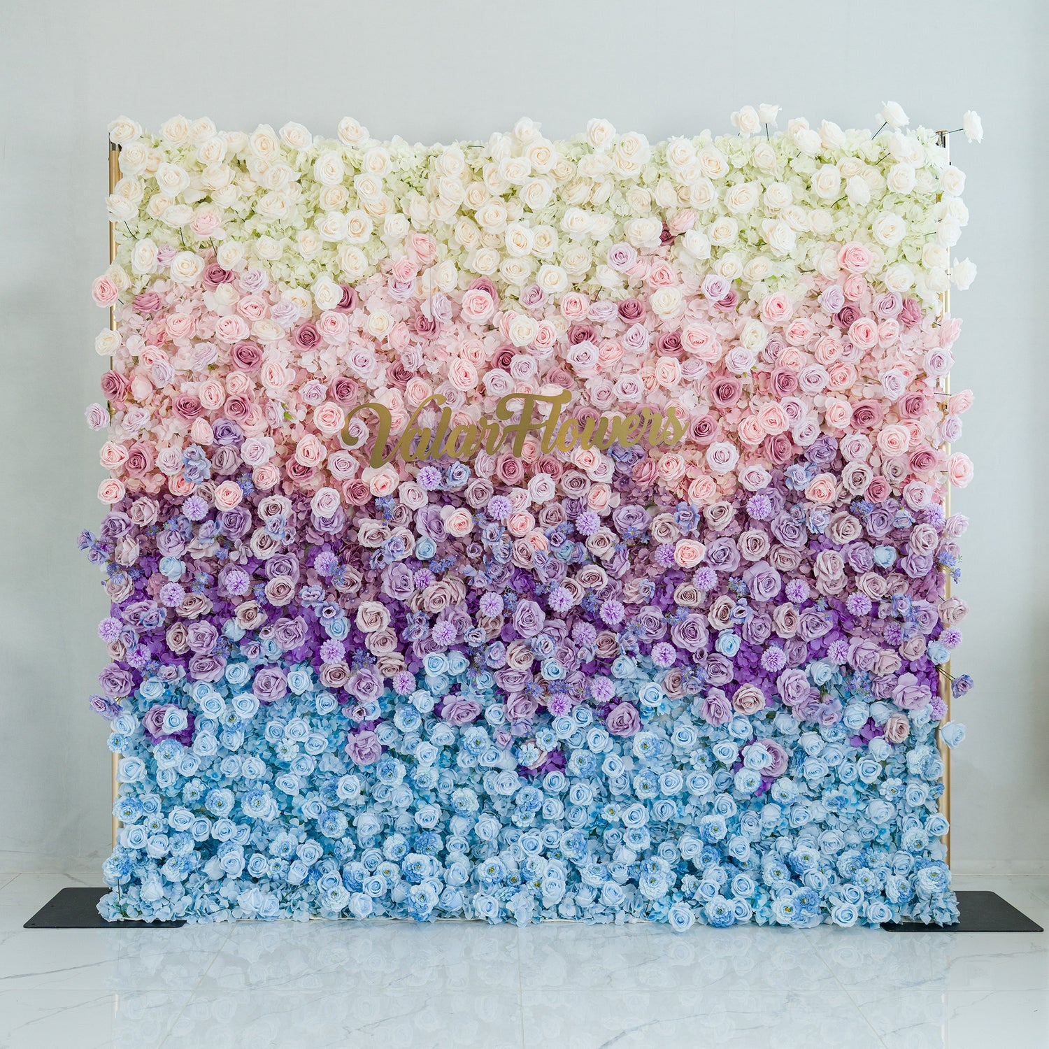 This stunning floral wall by ValarFlower showcases a gradient of blooms—white roses, pink peonies, purple hydrangeas, and blue blossoms. The color theme, transitioning from white to blue through soft pastels, creates a dreamy, elegant vibe. Perfect for weddings, galas, or upscale events, it blends romance and sophistication, ideal as a photo backdrop or decorative centerpiece.