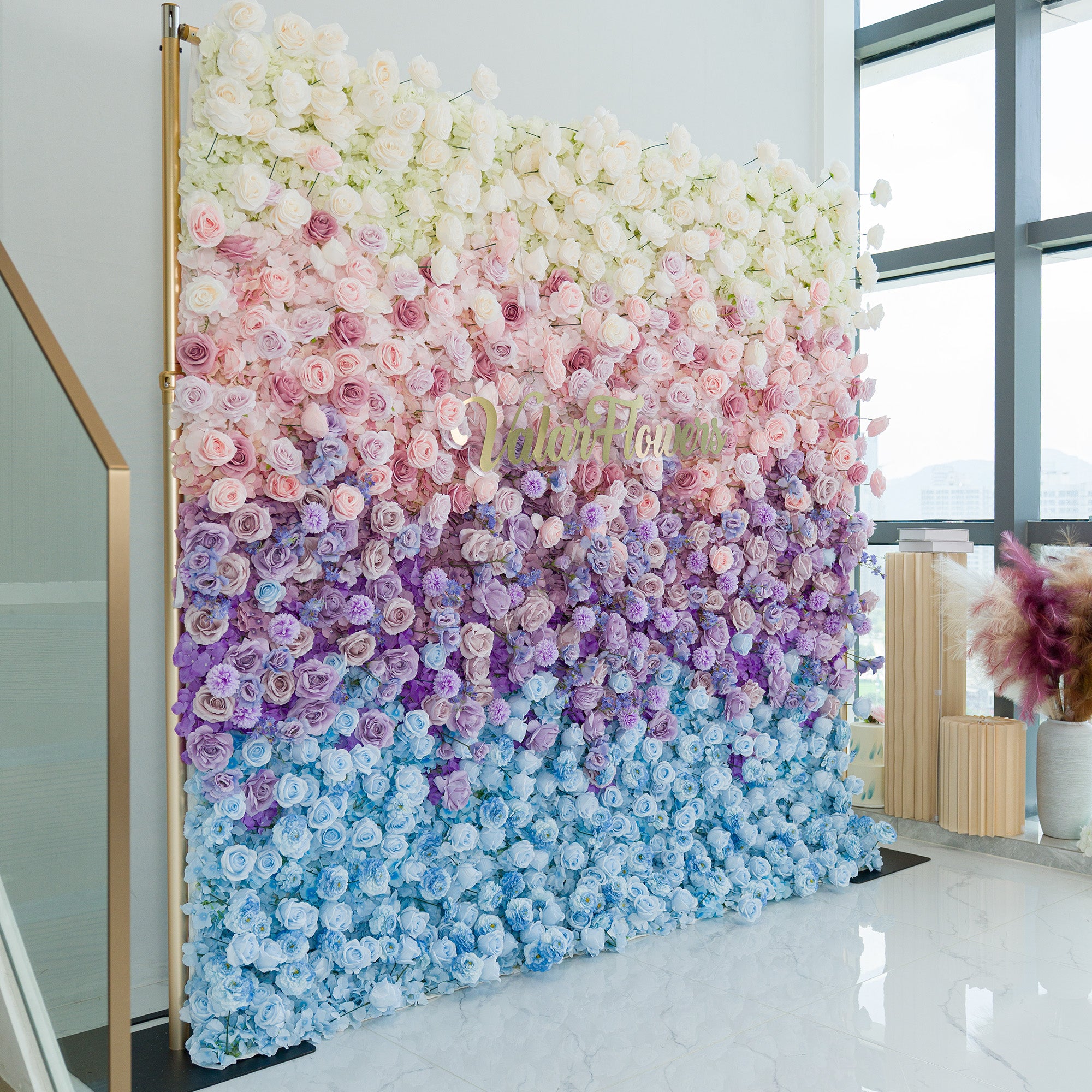 A captivating floral wall by ValarFlowers showcases a gradient of blooms—white roses, pink peonies, purple hydrangeas, and blue blossoms. The color theme transitions from soft pastels to deeper hues, creating a dreamy, elegant vibe. Set against a minimalist backdrop, it’s perfect for weddings, events, or photo backdrops, blending romance and sophistication in a lush, eye - catching display.