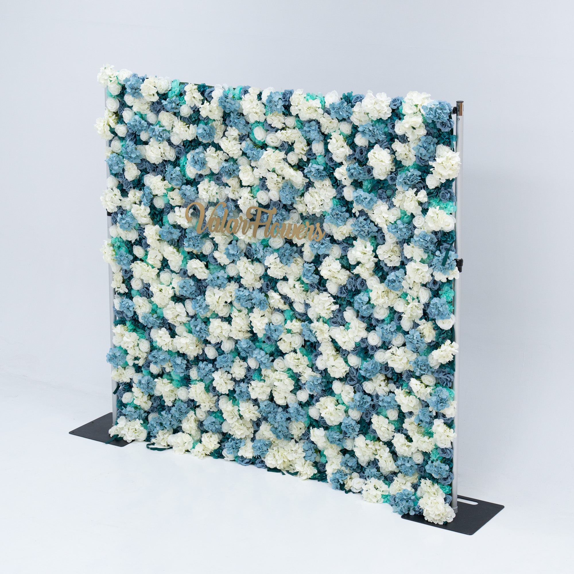 The backdrop is set against a plain white background, creating a clean and elegant look. The gold lettering of "Valar Flowers" adds a touch of sophistication, making it an ideal decorative piece for weddings, photo shoots, or other special events. The roses are meticulously arranged to create a visually appealing pattern, enhancing the overall aesthetic of the backdrop. This floral backdrop is perfect for events with a blue and white color theme, adding a touch of natural beauty and elegance to any setting.