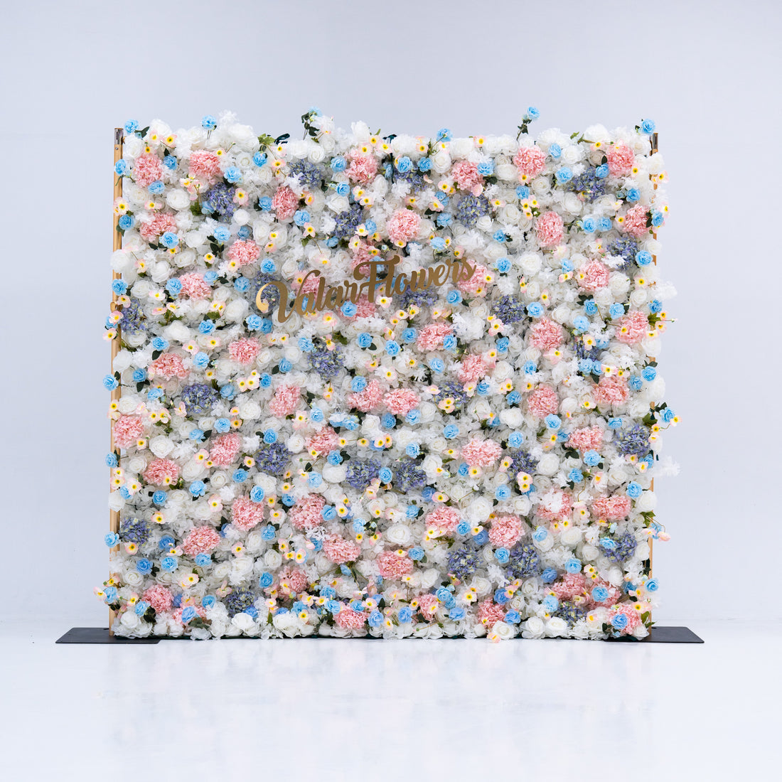 This photo features a stunning floral backdrop from Valar Flowers, showcasing a dense arrangement of artificial flowers in various shades of pink, blue, and white. The gold lettering of "ValarFlowers" adds a touch of elegance, making it an ideal decorative piece for weddings, photo shoots, or other special events. The meticulous arrangement of the flowers enhances the overall aesthetic, adding a touch of natural beauty and charm to any setting.