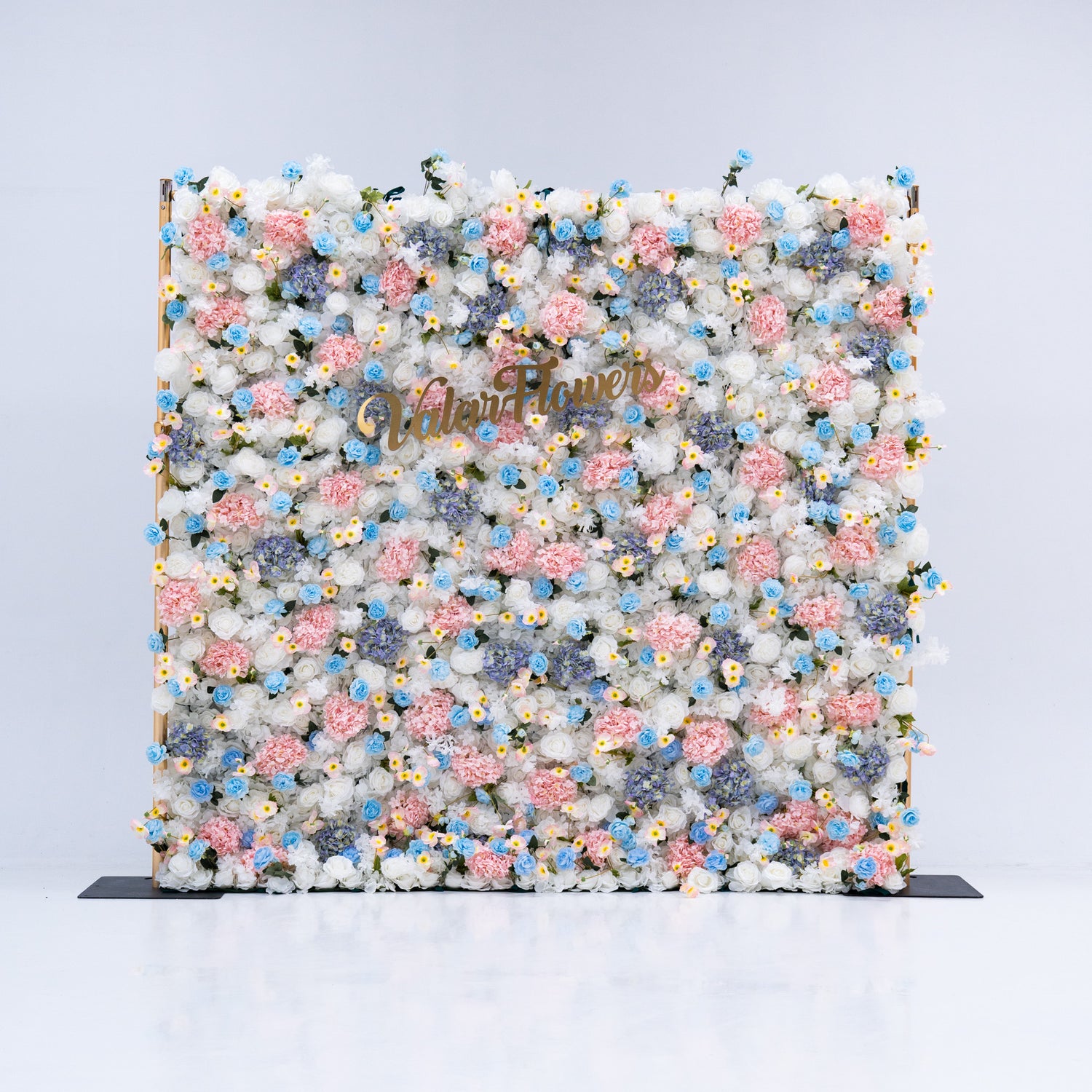 This photo features a stunning floral backdrop from Valar Flowers, showcasing a dense arrangement of artificial flowers in various shades of pink, blue, and white. The gold lettering of "ValarFlowers" adds a touch of elegance, making it an ideal decorative piece for weddings, photo shoots, or other special events. The meticulous arrangement of the flowers enhances the overall aesthetic, adding a touch of natural beauty and charm to any setting.