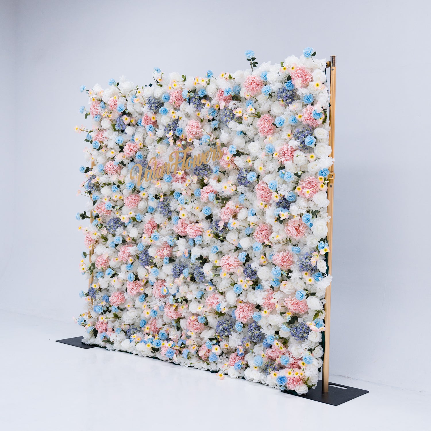 This photo showcases a magnificent floral backdrop from Valar Flowers, featuring a dense arrangement of artificial flowers in various shades of pink, blue, and white. The gold lettering of "ValarFlowers" adds a touch of elegance and sophistication, making it an ideal decorative piece for weddings, photo shoots, or other special events. The meticulous arrangement of the flowers enhances the overall aesthetic, adding a touch of natural beauty and charm to any setting.