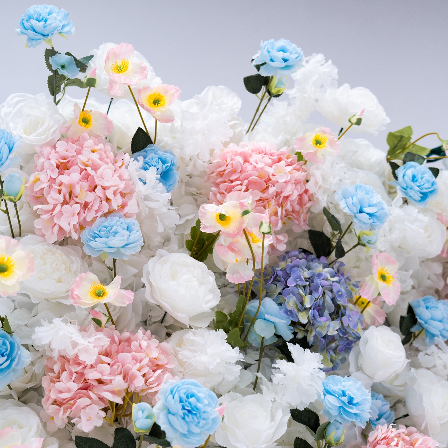 This photo showcases a beautiful arrangement of artificial flowers, featuring white and blue roses alongside pink and blue hydrangeas. The flowers are densely packed, creating a visually appealing and vibrant display. This floral backdrop is perfect for weddings, photo shoots, or other special events, adding a touch of sophistication and natural beauty to any setting.