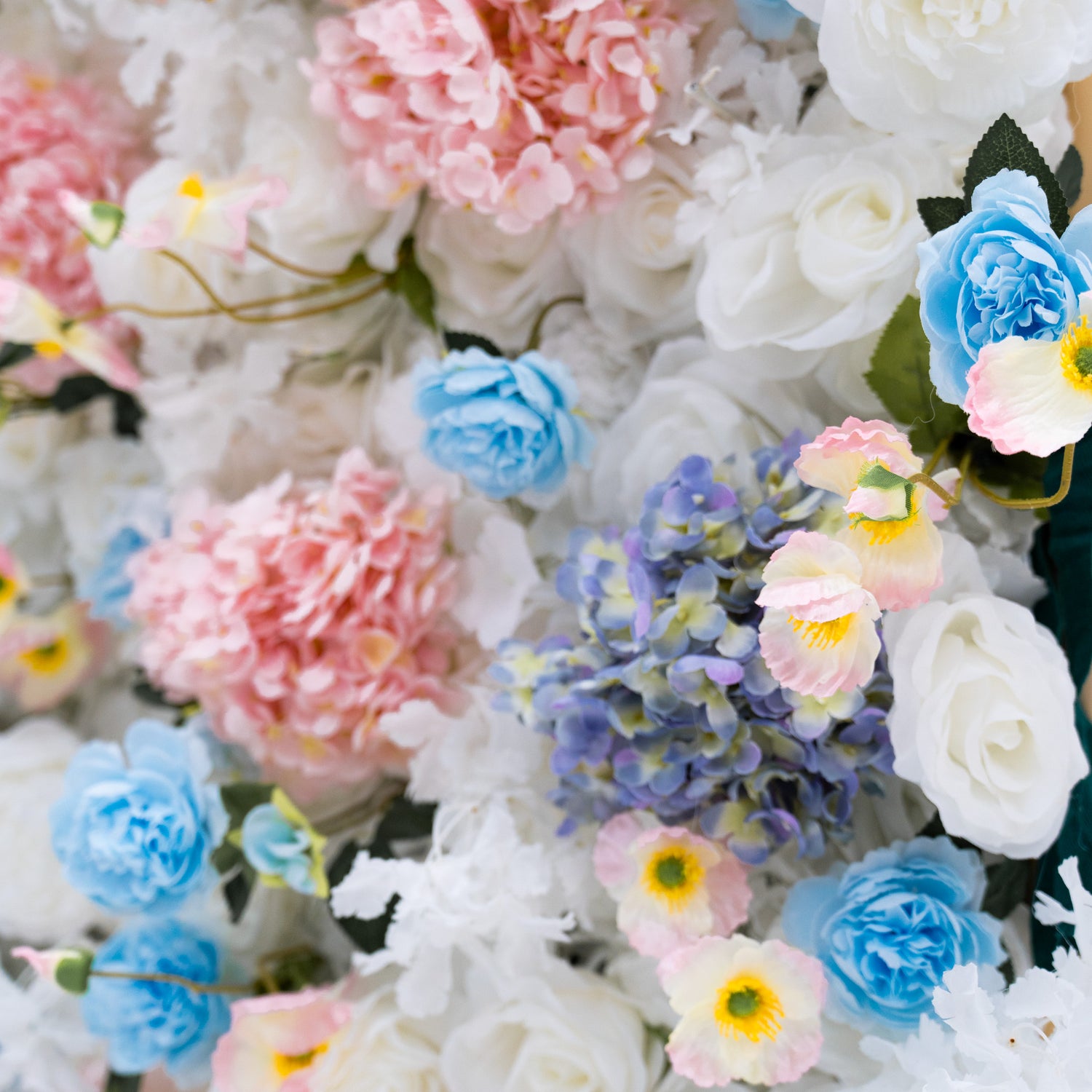 This photo features a lush arrangement of artificial flowers, including white and blue roses, and pink and blue hydrangeas. The flowers are densely packed, creating a visually appealing and vibrant display. This floral backdrop is perfect for weddings, photo shoots, or other special events, adding a touch of sophistication and natural beauty to any setting.