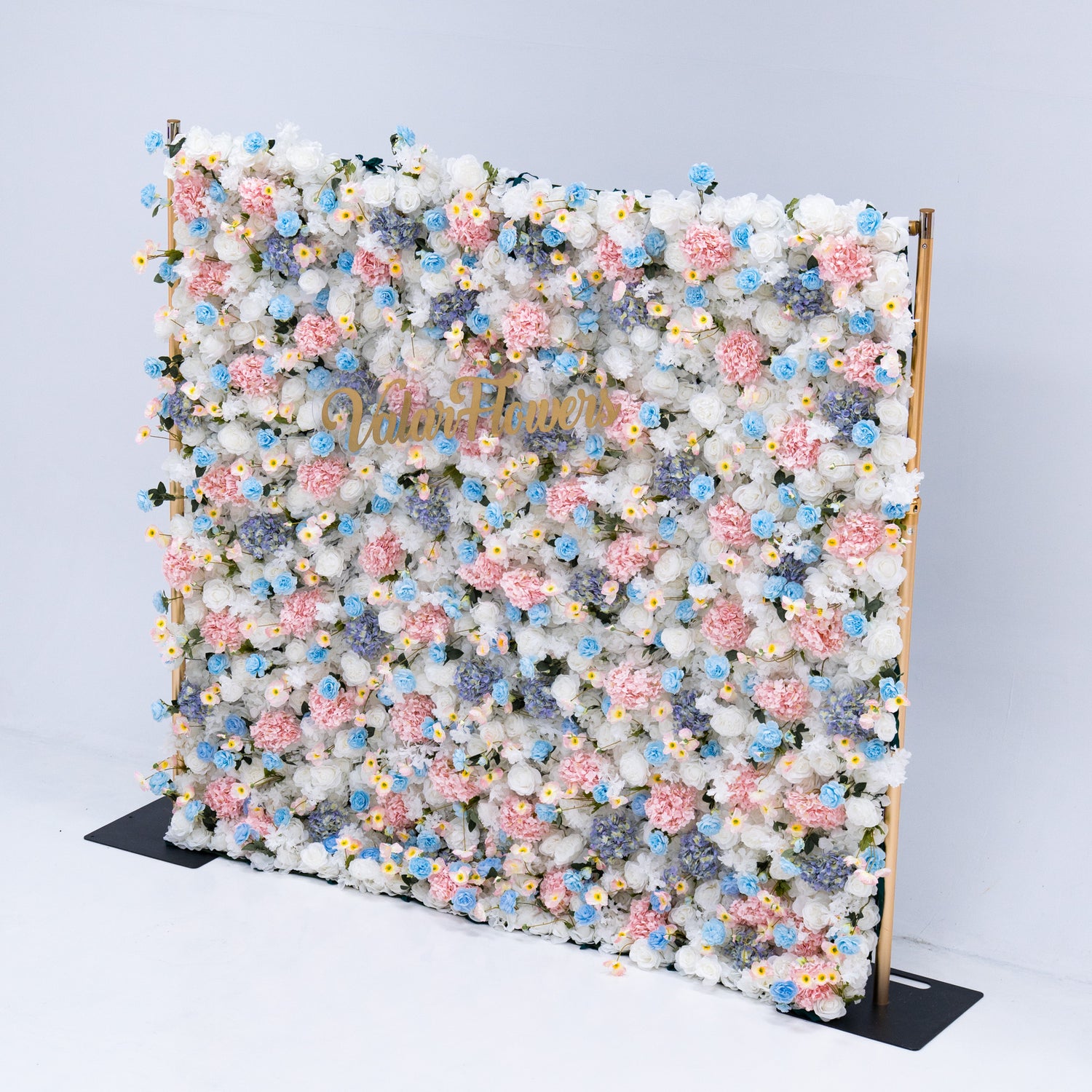 This photo showcases a magnificent floral backdrop from Valar Flowers, featuring a dense arrangement of artificial flowers in various shades of pink, blue, and white. The gold lettering of "Valar Flowers" adds a touch of elegance and sophistication, making it an ideal decorative piece for weddings, photo shoots, or other special events. The meticulous arrangement of the flowers enhances the overall aesthetic, adding a touch of natural beauty and charm to any setting.