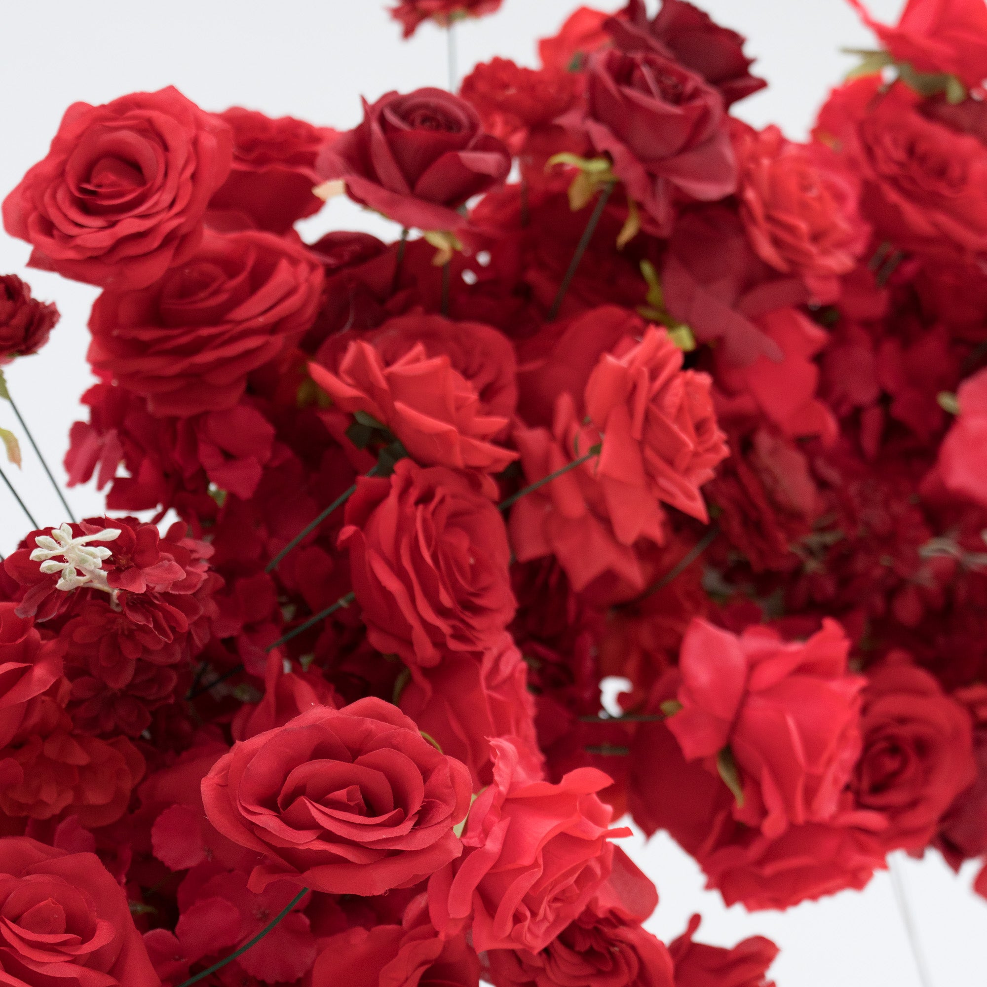 A dense cluster of artificial red roses, showcasing various shades from bright to deep crimson. The blooms, with their velvety petals and green stems, create a lush, romantic arrangement. Perfect for decorative purposes, adding a touch of elegance and passion to any setting.