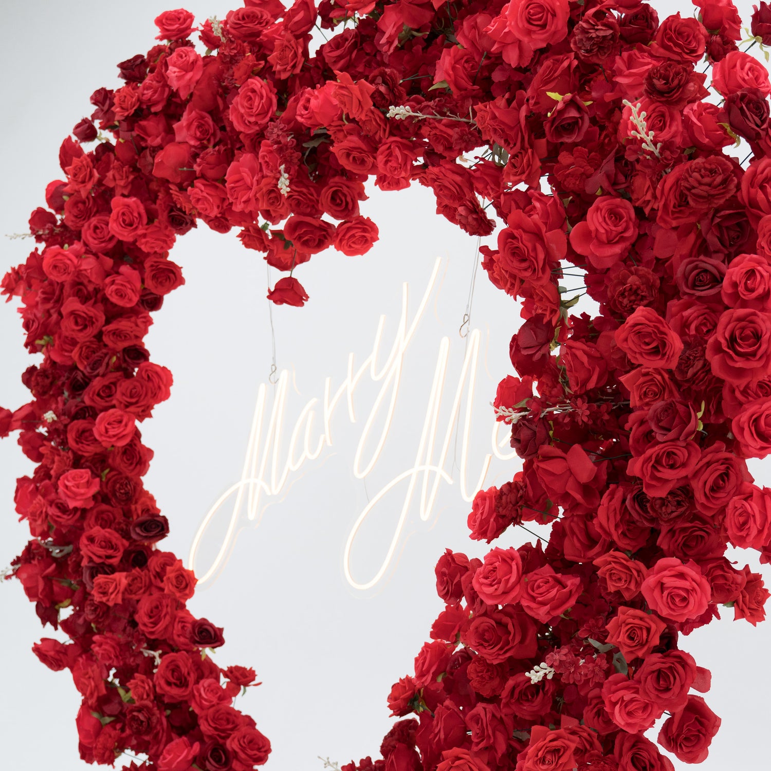 A romantic heart - shaped wreath made of lush red roses frames a glowing “Marry Me” neon sign. The vibrant blooms and soft lighting create an intimate, proposal - perfect atmosphere, blending floral beauty with a heartfelt message.
