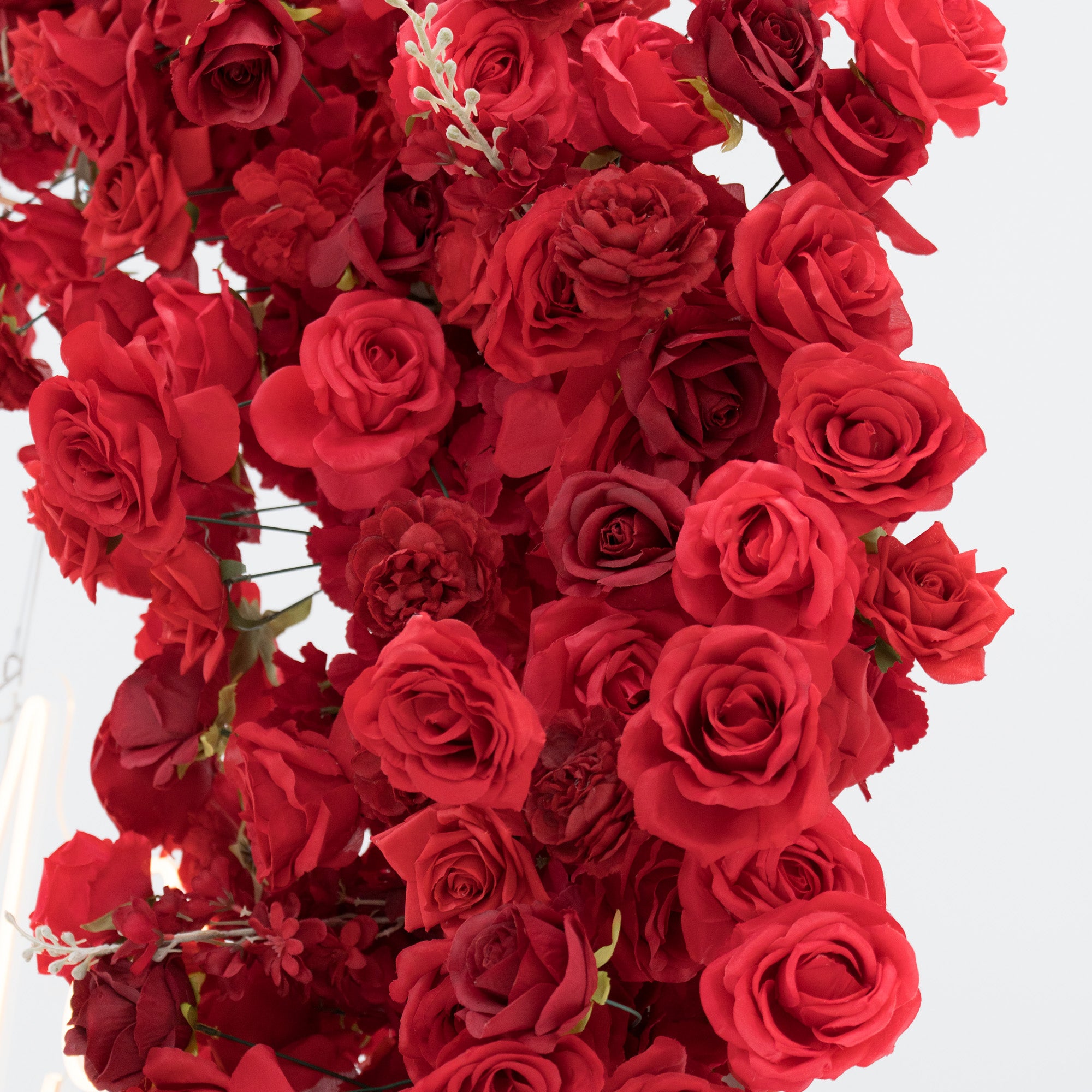 A dense cluster of artificial red roses in varying shades, with lush petals and green stems. The vibrant, uniform blooms create a rich, romantic texture, ideal for decorative displays, adding an elegant and passionate touch to any setting.