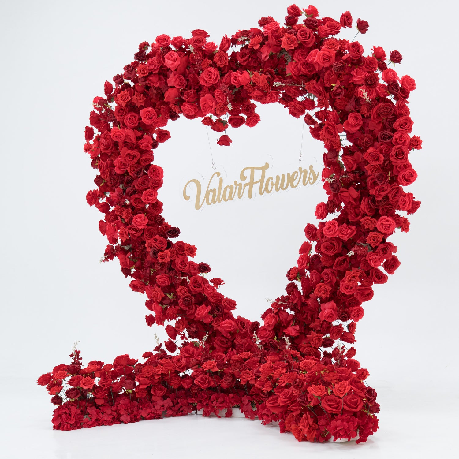 A woman in a black one - shoulder top and blue jeans stands beside a huge heart - shaped red rose installation. At its center, a glowing “Marry Me” sign adds a romantic touch. The lush, vibrant blooms create a striking, proposal - worthy scene.