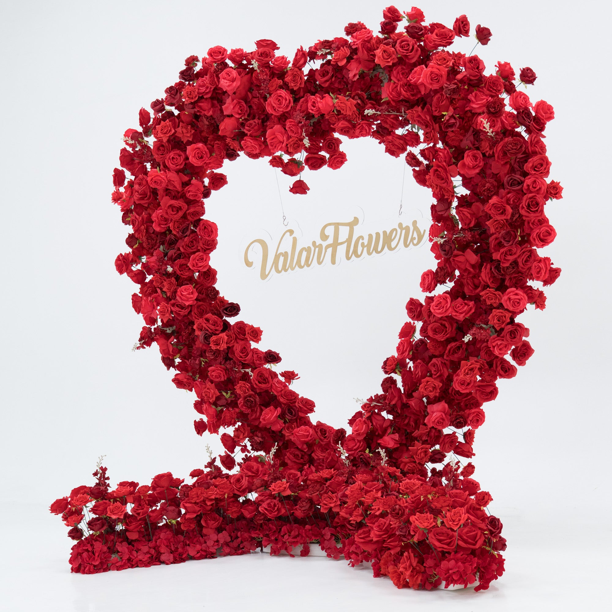 A woman in a black one - shoulder top and blue jeans stands beside a huge heart - shaped red rose installation. At its center, a glowing “Marry Me” sign adds a romantic touch. The lush, vibrant blooms create a striking, proposal - worthy scene.