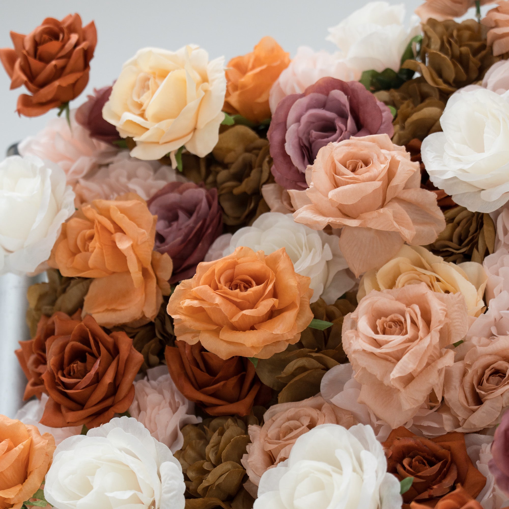 A close - up of artificial roses in warm tones—beige, peach, brown, white, and purple. Their soft, layered petals create a lush, textured arrangement, ideal for decorative backdrops or floral displays, evoking a romantic and elegant vibe.