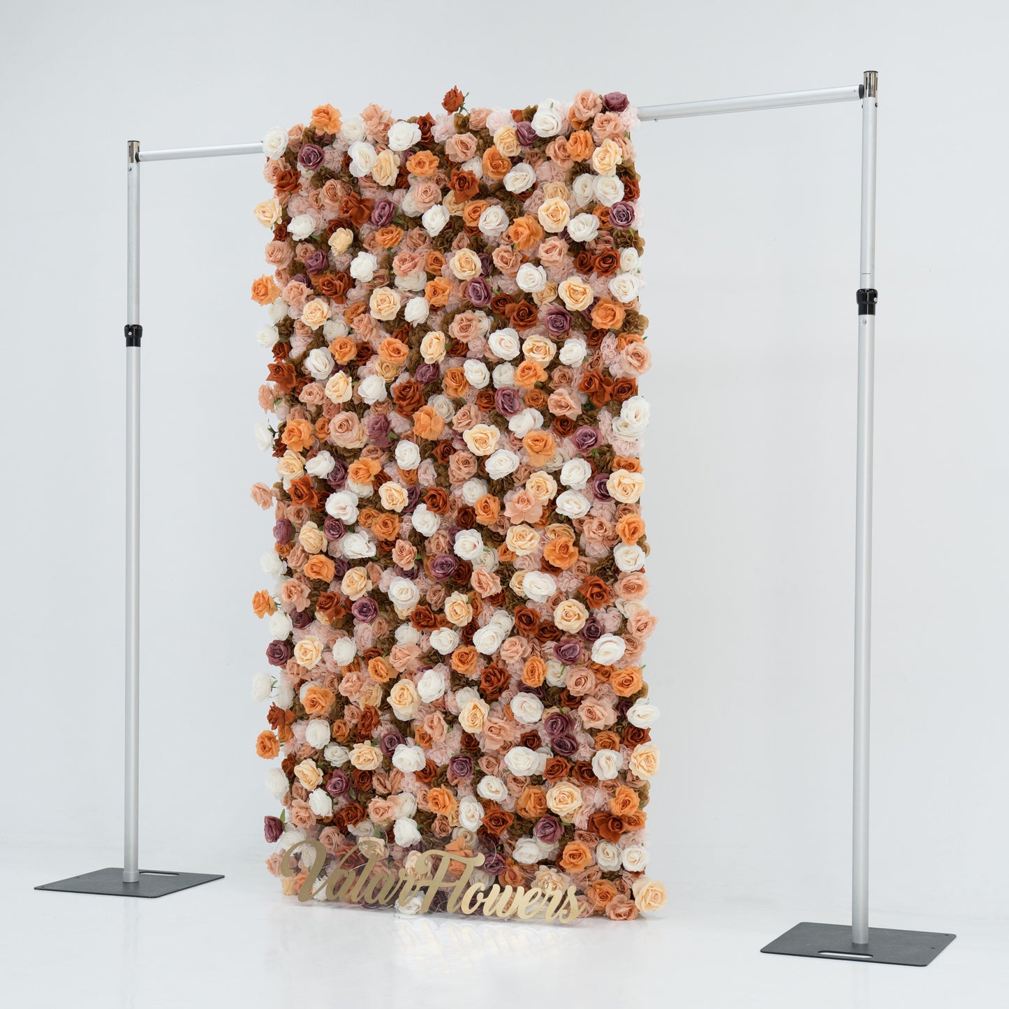 A tall, rectangular artificial flower wall features a mix of beige, white, peach, and purple roses. It’s mounted on a metal frame, with a gold “ValarFlowers” sign at the bottom. The dense, varied blooms create an elegant, textured backdrop for events or decor.