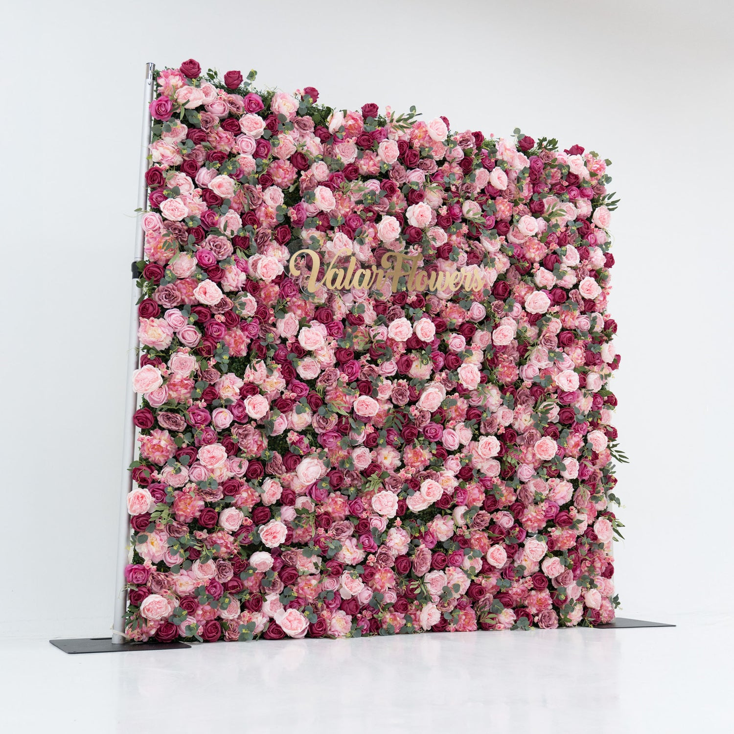 A large artificial flower wall bursts with pink and deep - pink roses, interspersed with green foliage. A gold “ValarFlowers” sign stands out, creating a romantic, elegant backdrop—ideal for events, exuding charm and sophistication.