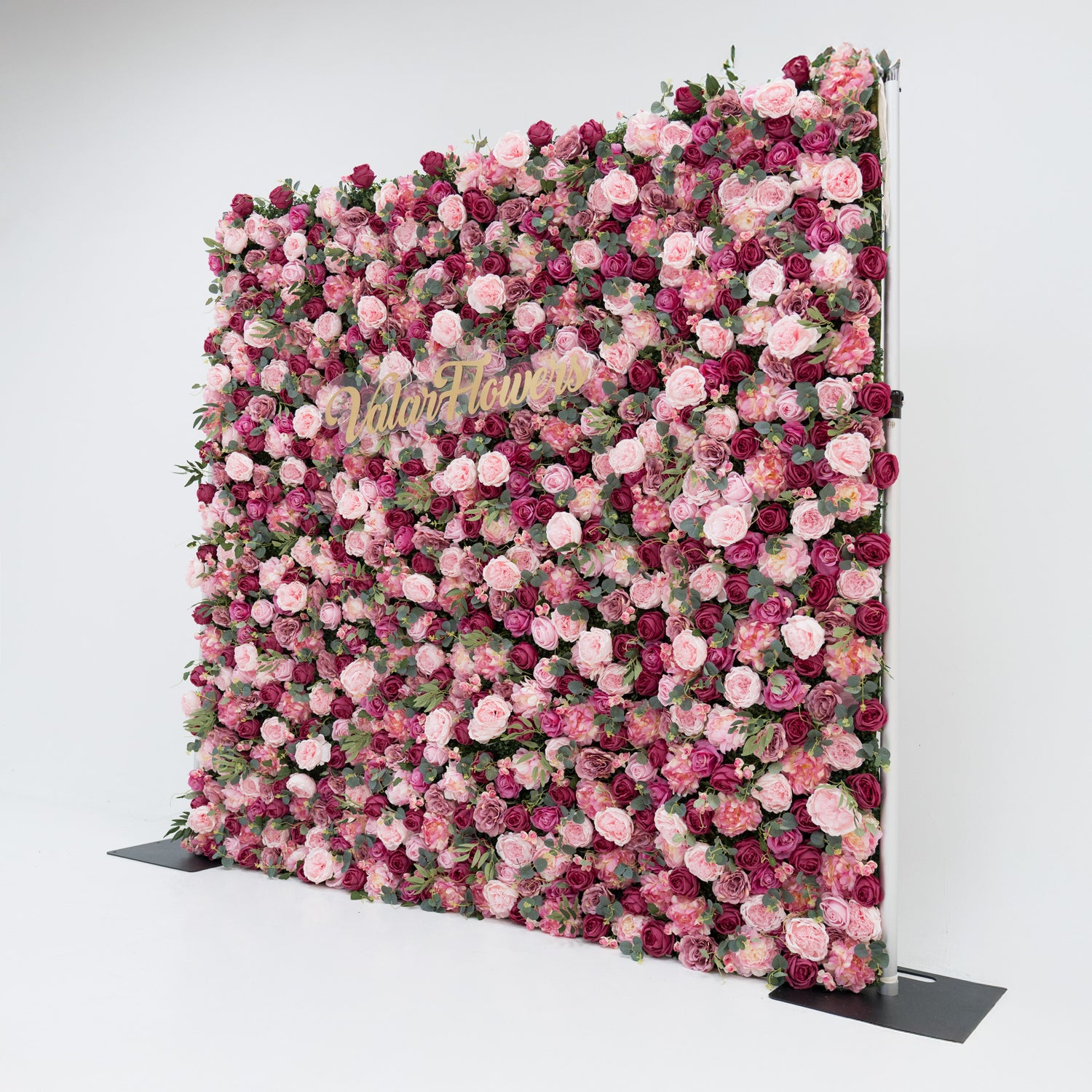 A large artificial flower wall, a vibrant mix of pink, deep - pink roses, and green foliage. A gold “ValarFlowers” sign is centrally placed, creating a romantic, elegant backdrop—ideal for events, exuding charm and sophistication with its lush, colorful blooms.