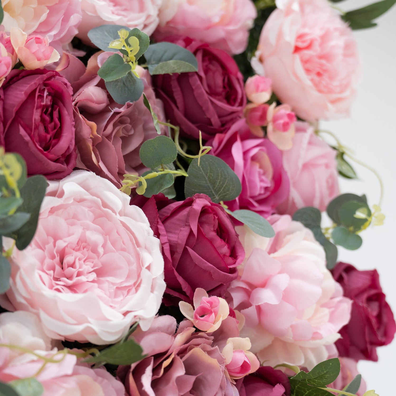 A close - up of artificial flowers: soft pink peonies, deep - red roses, and delicate buds, all interspersed with green foliage. The lush, layered petals and varied hues create a romantic, realistic arrangement—perfect for decorative displays, adding charm and elegance.