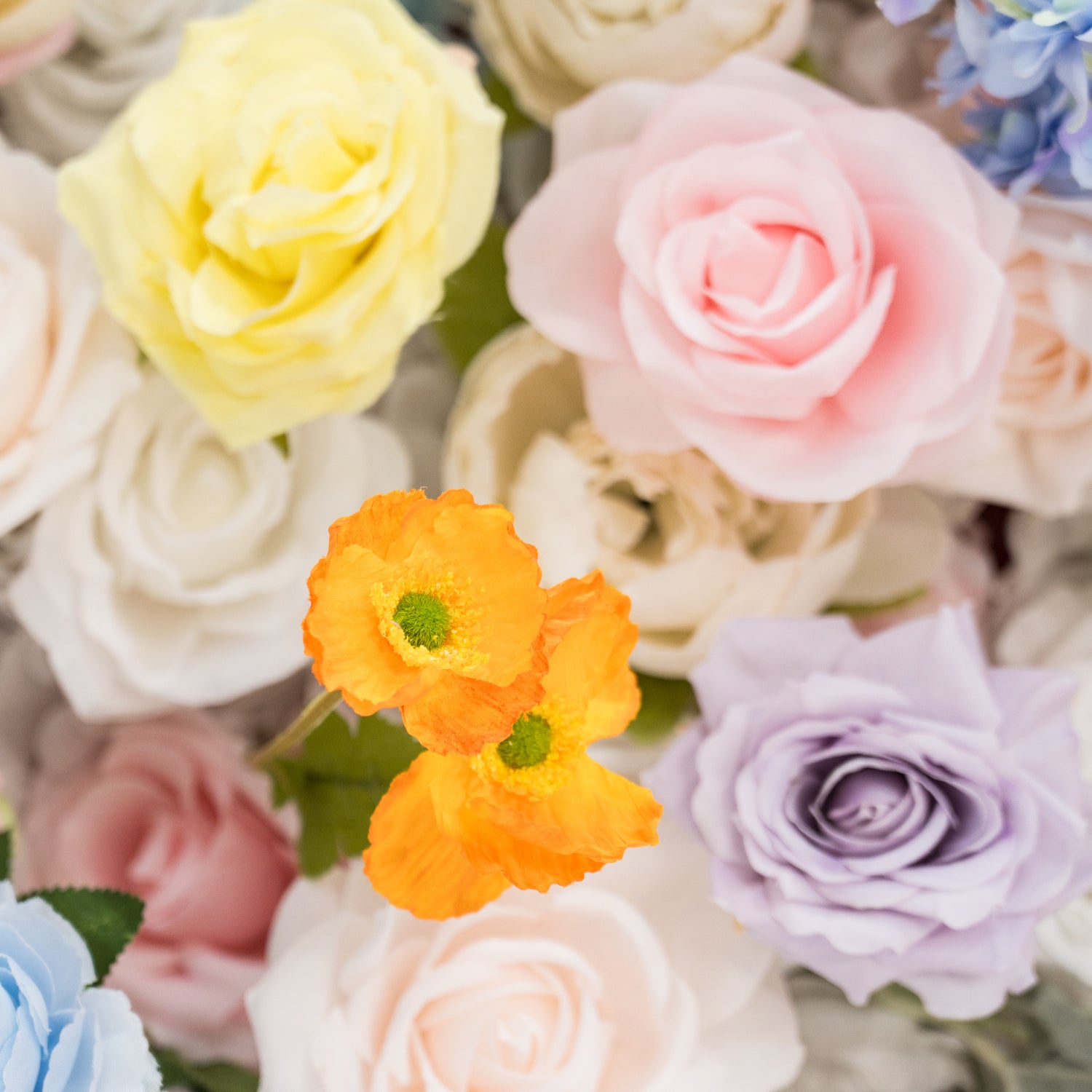 A vibrant arrangement of artificial flowers showcases a lovely mix of colors. There are soft yellow, pink, and purple roses, along with two bright orange flowers with green centers. The petals have a smooth, realistic texture, creating a delicate and charming floral display. Set against a backdrop of other pastel - hued blooms, it exudes a cheerful and elegant vibe, perfect for decorative purposes.