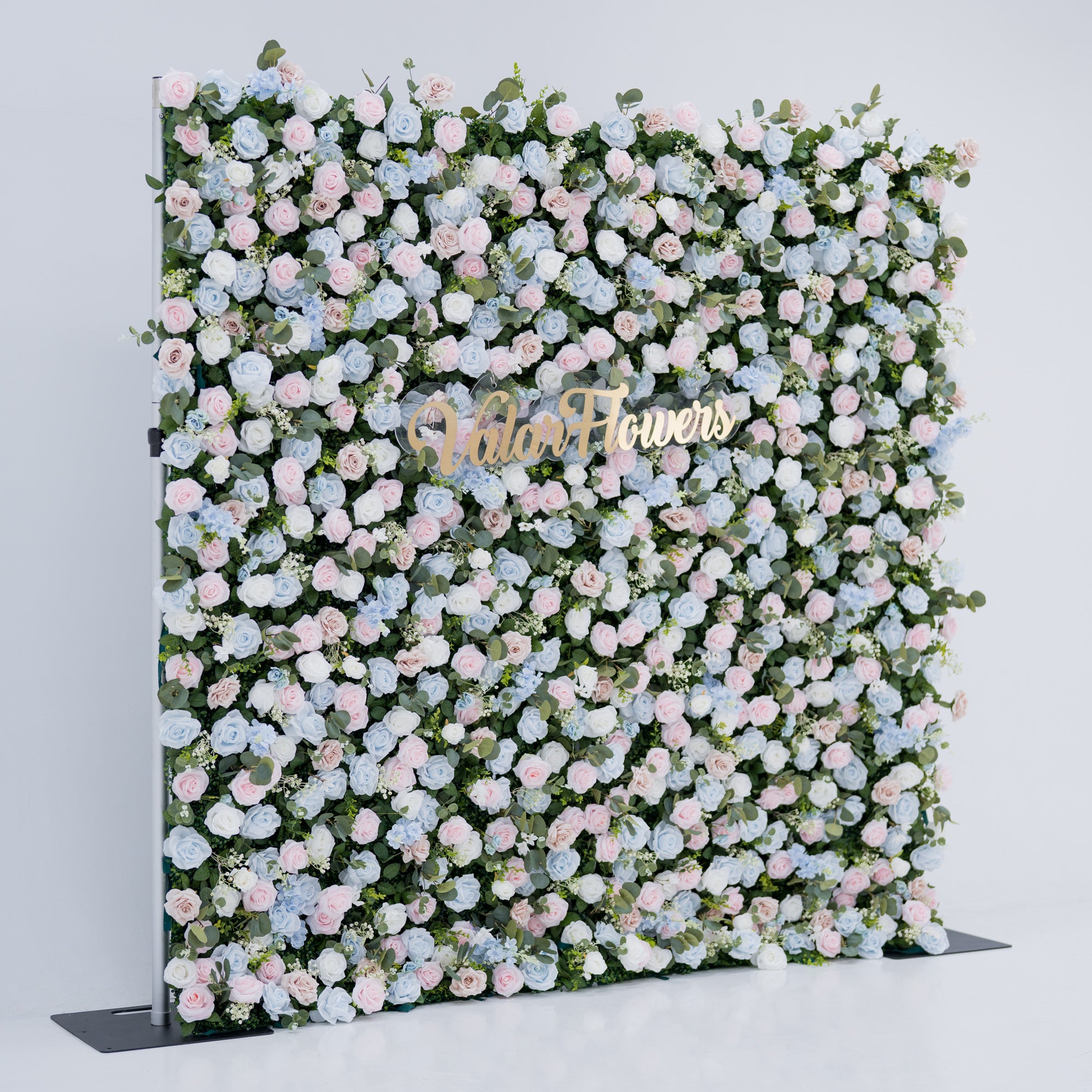 This image showcases a vibrant floral backdrop by Valar Flowers, set against a plain white indoor background. It features a dense arrangement of artificial flowers in various shades of blue, light blue, and pink, with the brand’s name elegantly integrated in gold. Exuding elegance, it’s perfect for adding a sophisticated, nature-inspired element to events or interiors, highlighting Valar Flowers’ craftsmanship in detailed, eye-catching decor.