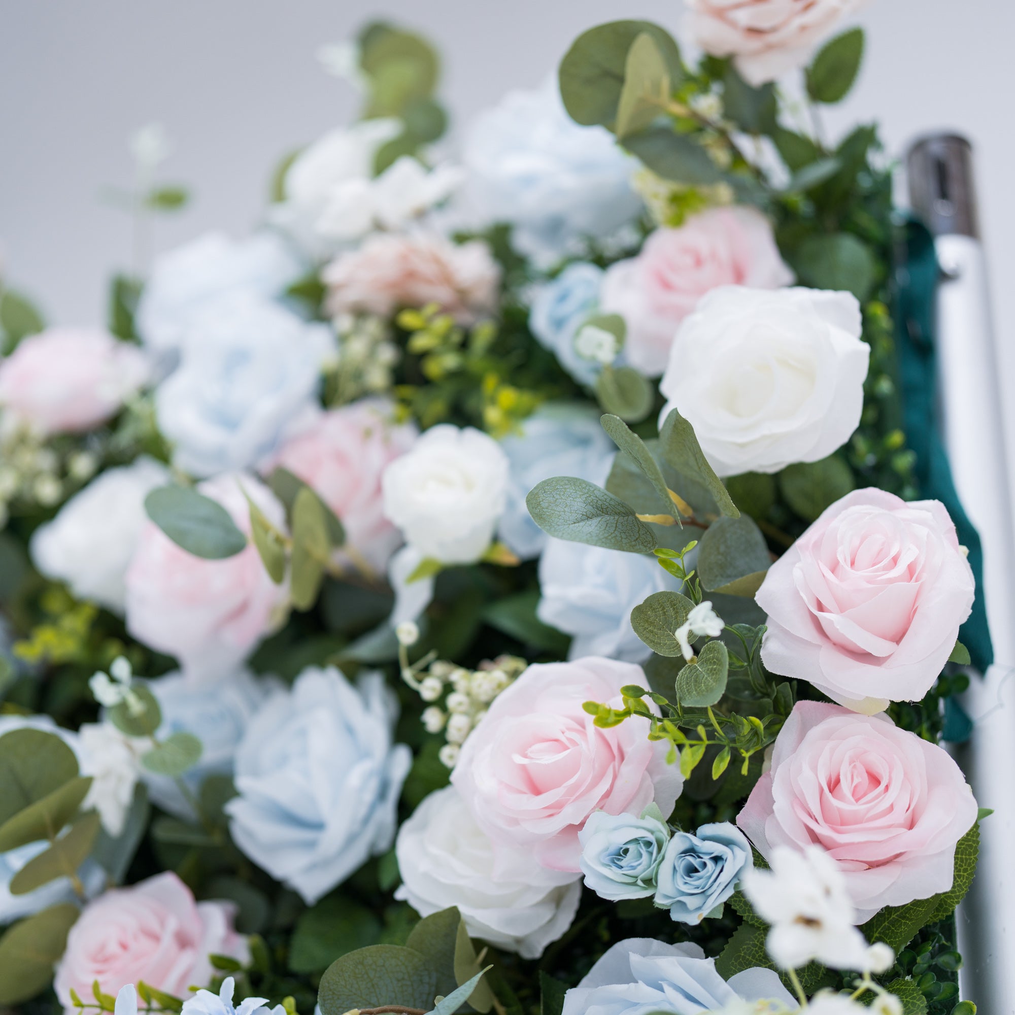 This image showcases a vibrant section of a floral backdrop by Valar Flowers, featuring a dense arrangement of artificial flowers in shades of pink, light blue, and white. Complemented by green foliage like eucalyptus, it exudes elegance and is perfect for adding a sophisticated, nature-inspired element to events, highlighting Valar Flowers’ craftsmanship in detailed, eye-catching decor.