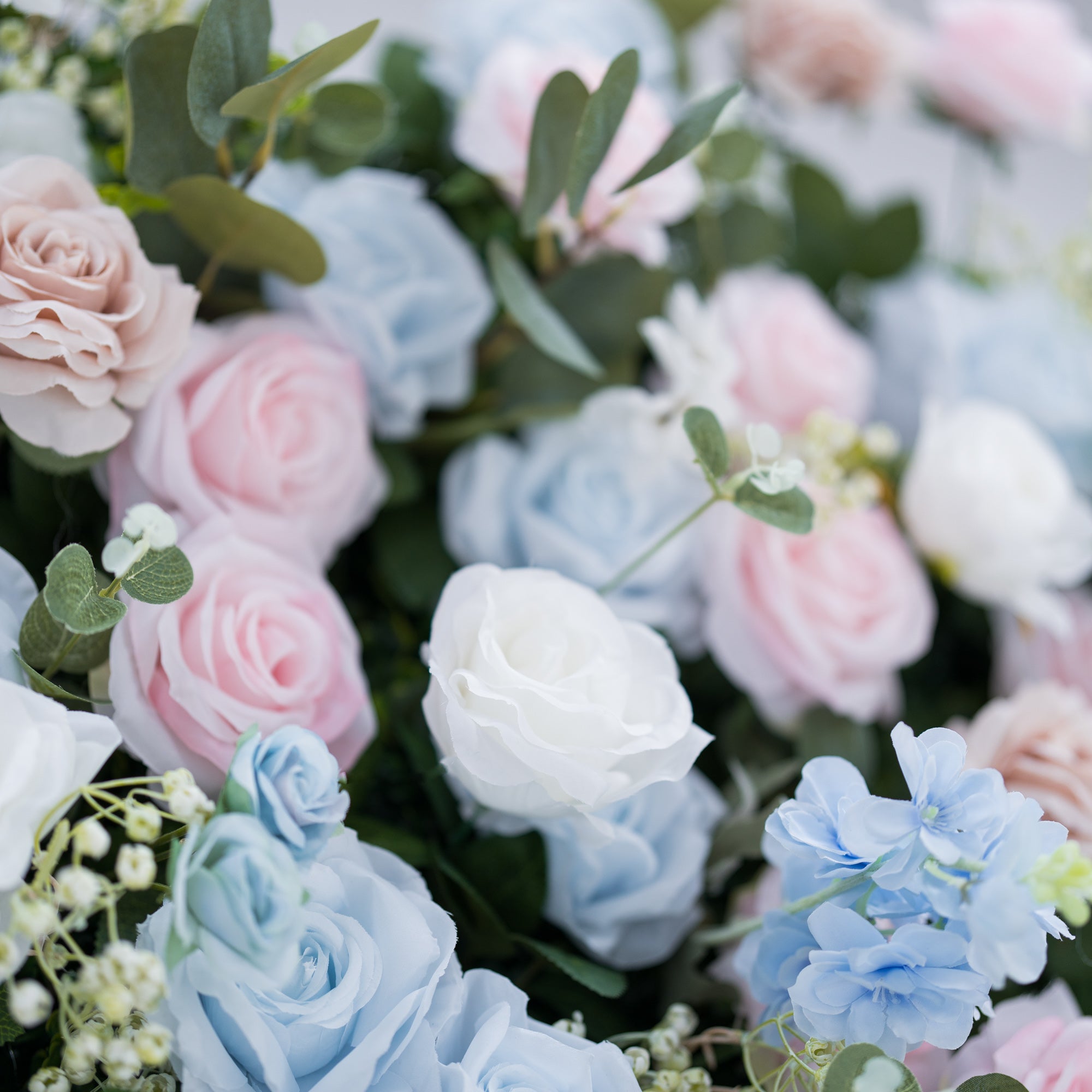 This image showcases a vibrant section of a floral backdrop by Valar Flowers, featuring a dense arrangement of artificial flowers in shades of light blue, pink, white, and blush. Complemented by green foliage like eucalyptus, it exudes elegance and is perfect for adding a sophisticated, nature-inspired element to events, highlighting Valar Flowers’ craftsmanship in detailed, eye-catching decor.