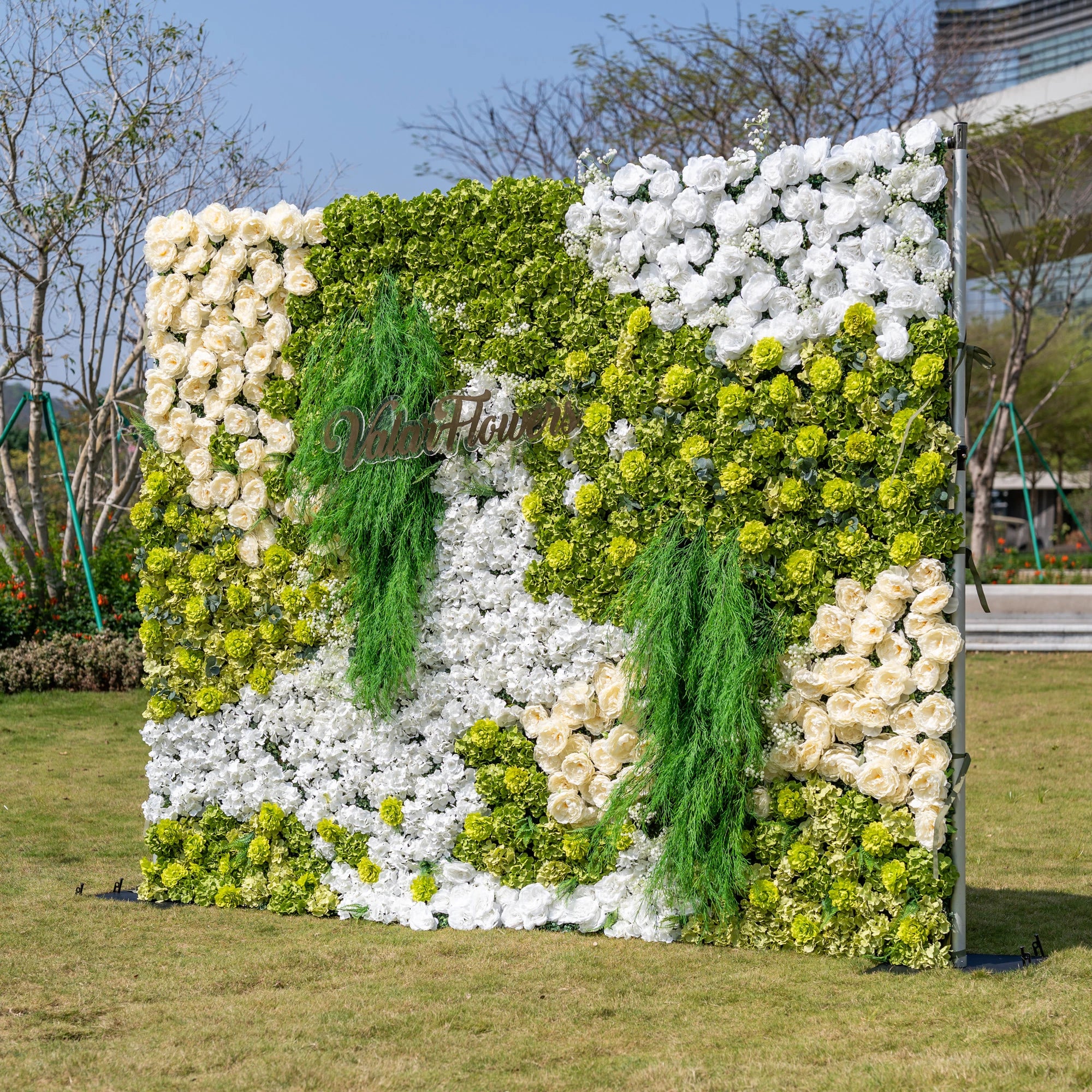 This is a premium nature-inspired artificial flower wall backdrop by Valar Flowers, featuring a lush, layered design with vibrant green hydrangeas, crisp white blooms, and soft ivory roses, accented by cascading green foliage. The custom "ValarFlowers" logo adds a personalized touch. This reusable, maintenance-free display creates a fresh, elegant focal point, ideal for outdoor weddings, garden parties, photo booths, and luxury events, offering long-lasting beauty for professional decor.