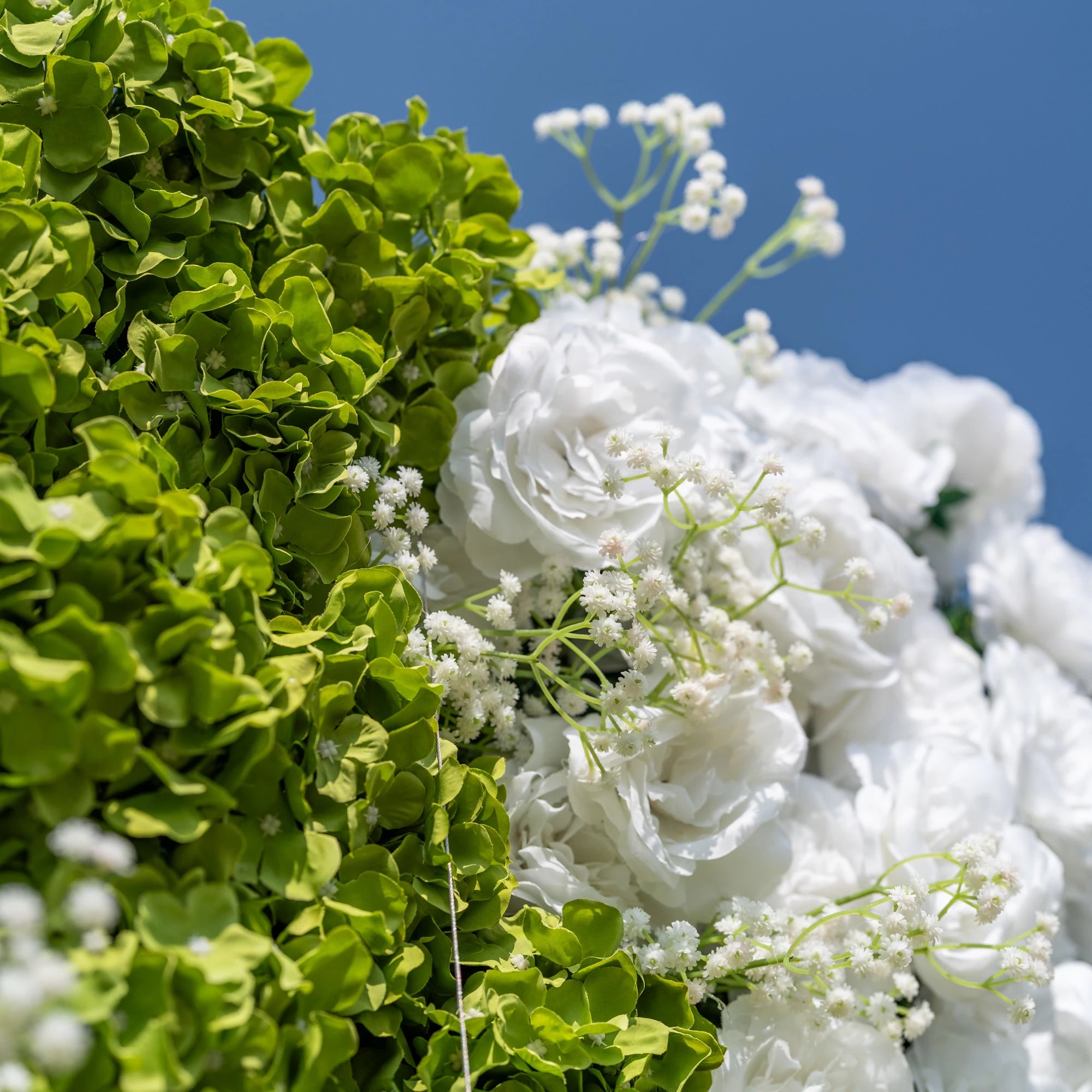 This close-up showcases Valar Flowers’ premium artificial floral wall, featuring lush, vibrant green hydrangeas, soft white roses, and delicate baby’s breath. The hyper-realistic petals and dense, layered foliage mimic fresh blooms, creating a lifelike, maintenance-free display. Ideal for wedding backdrops, photo booths, and luxury events, this durable, reusable decor offers a fresh, elegant aesthetic for professional styling.