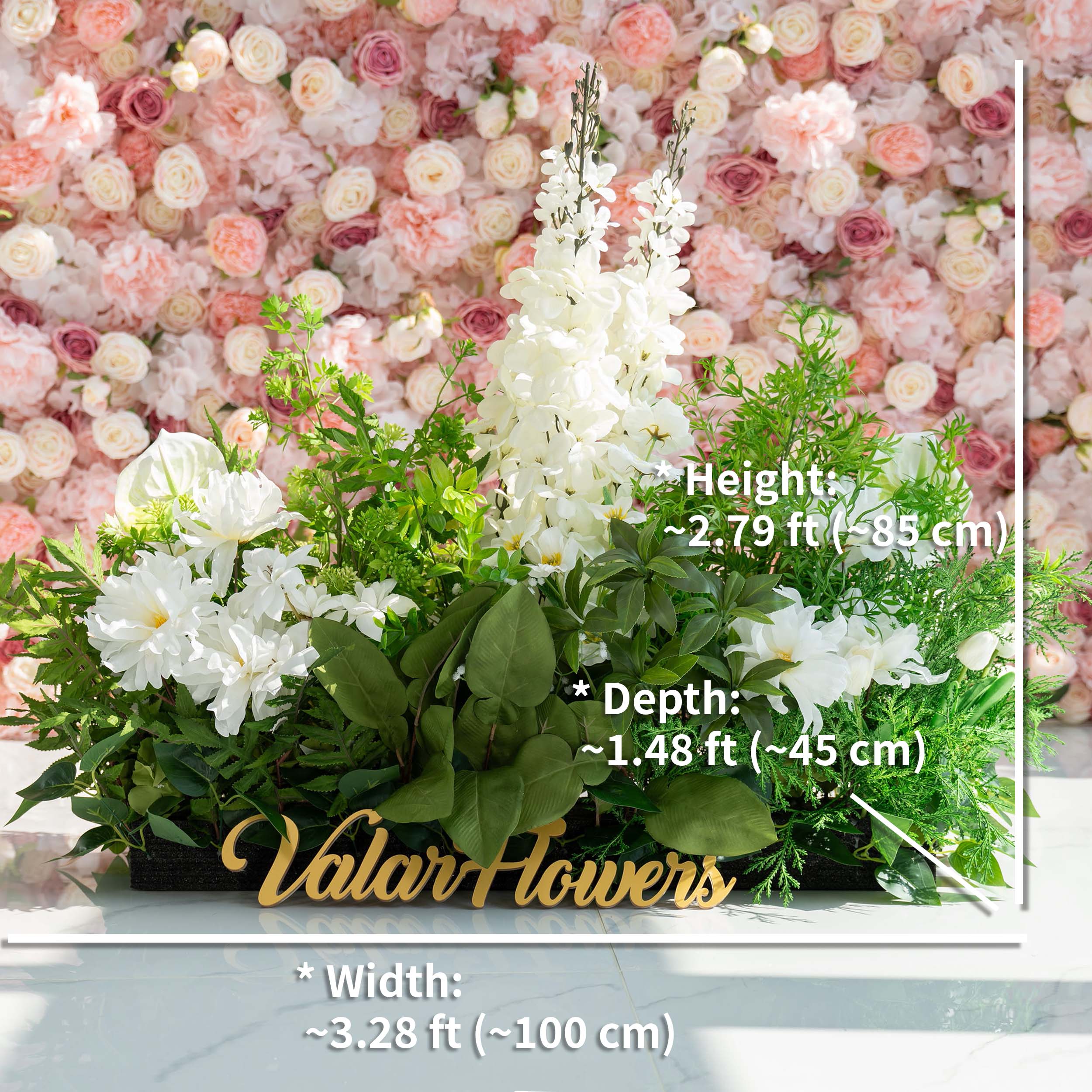 The floral arrangement features a variety of flowers, including white lilies, hydrangeas, and orchids, complemented by lush green foliage. It is ideal for weddings, creating a romantic and elegant atmosphere. The sign "Valar Flowers" adds a charming touch.