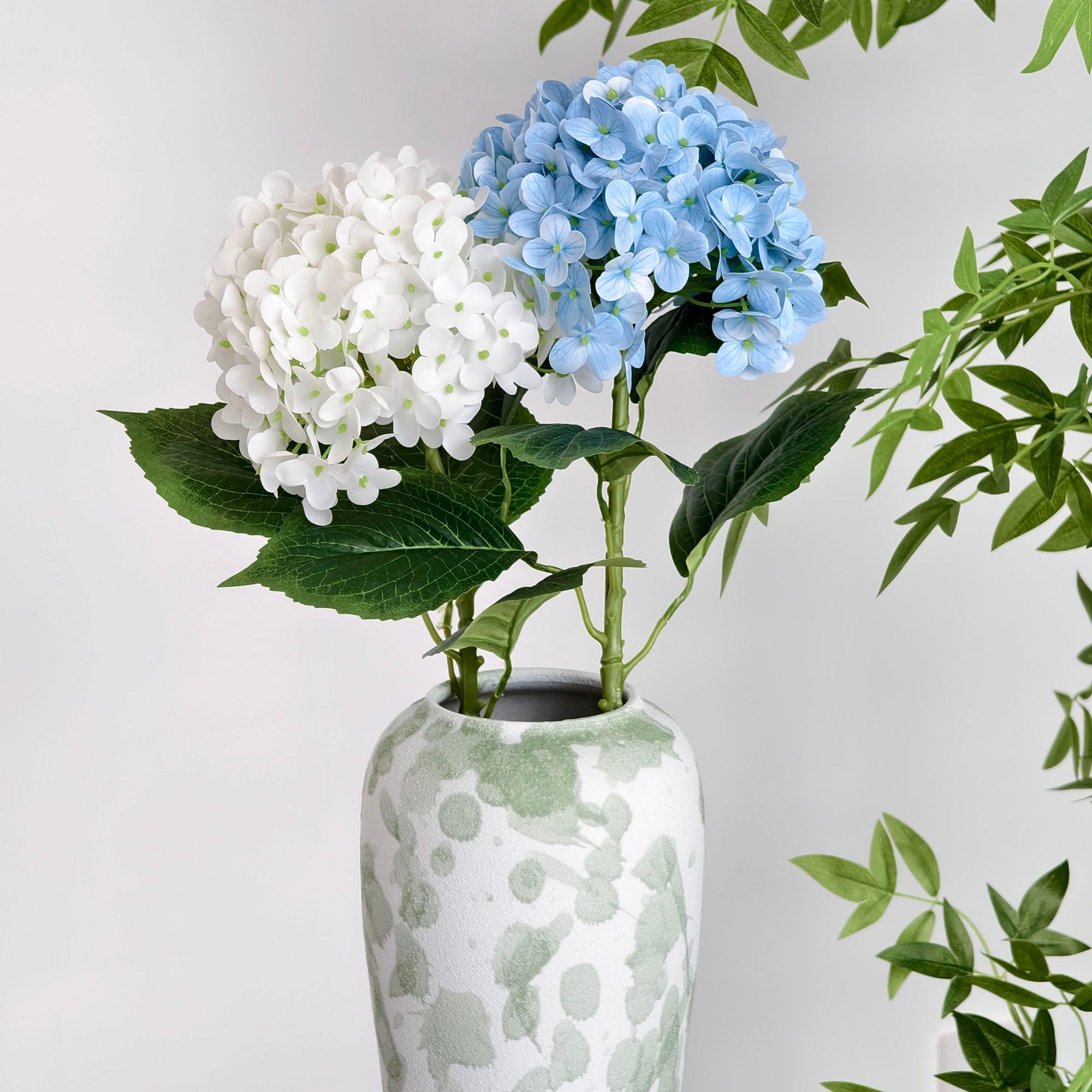 This arrangement features two artificial hydrangea blooms—one in deep pink, the other in soft pink—with green leaves, placed in a white vase with green watercolor - like patterns. The pastel hues and minimalist design create a gentle, elegant decor vibe, perfect for adding a touch of natural beauty to any space.