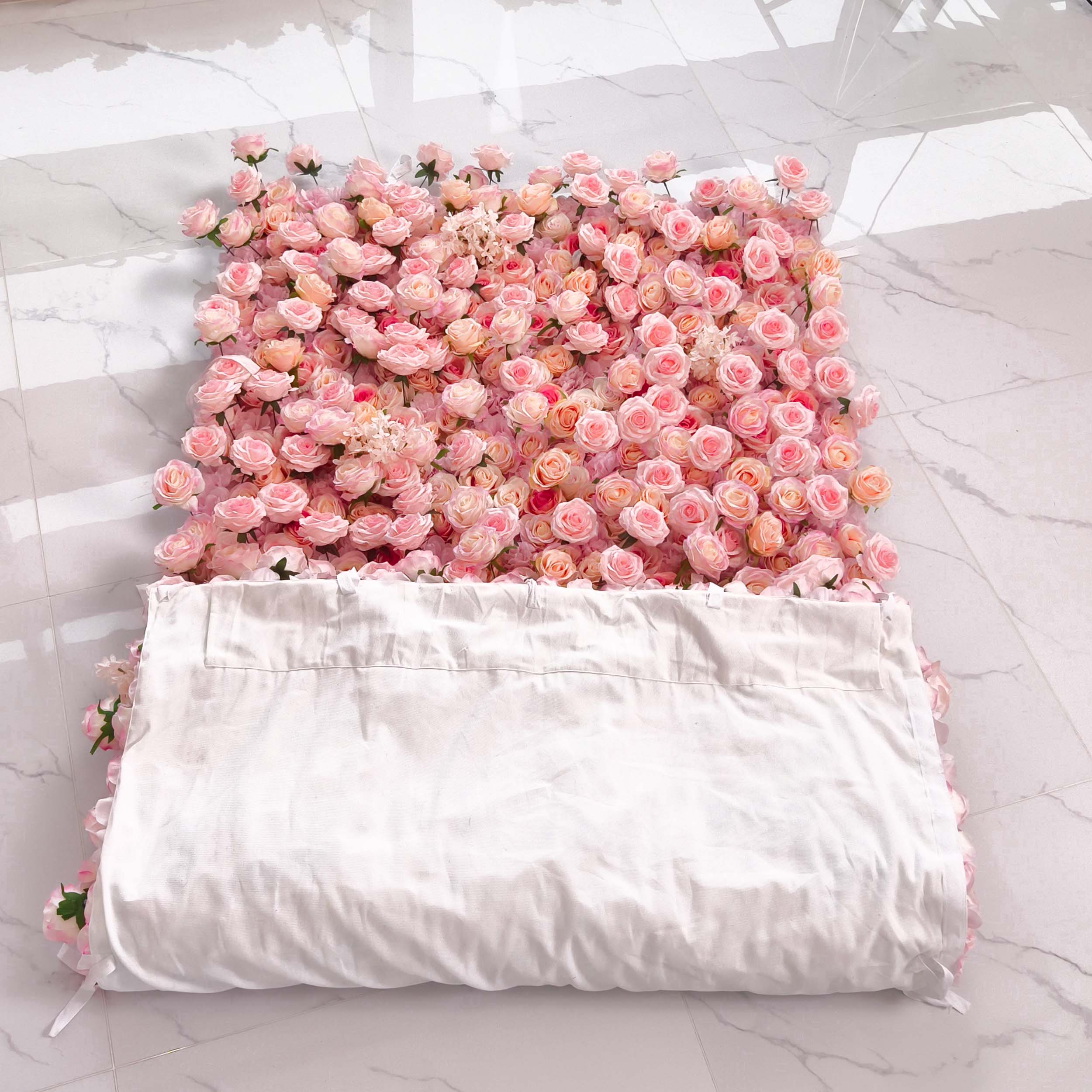A 4x8ft square of artificial pink roses lies on the floor. Partially covered by a white sheet, the roses create a soft, romantic look. The marble floor adds a touch of elegance.