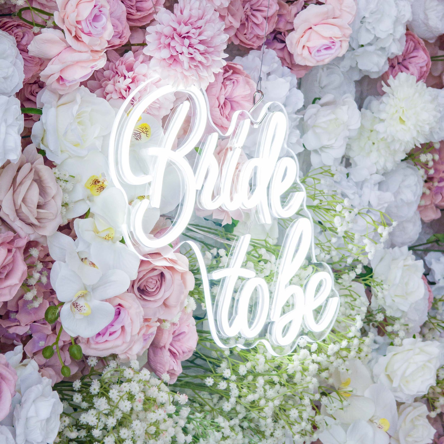 This backdrop is a lush floral arrangement with a romantic and feminine style. It features a mix of artificial flowers, including roses in soft pinks and whites, white orchids, and clusters of baby&