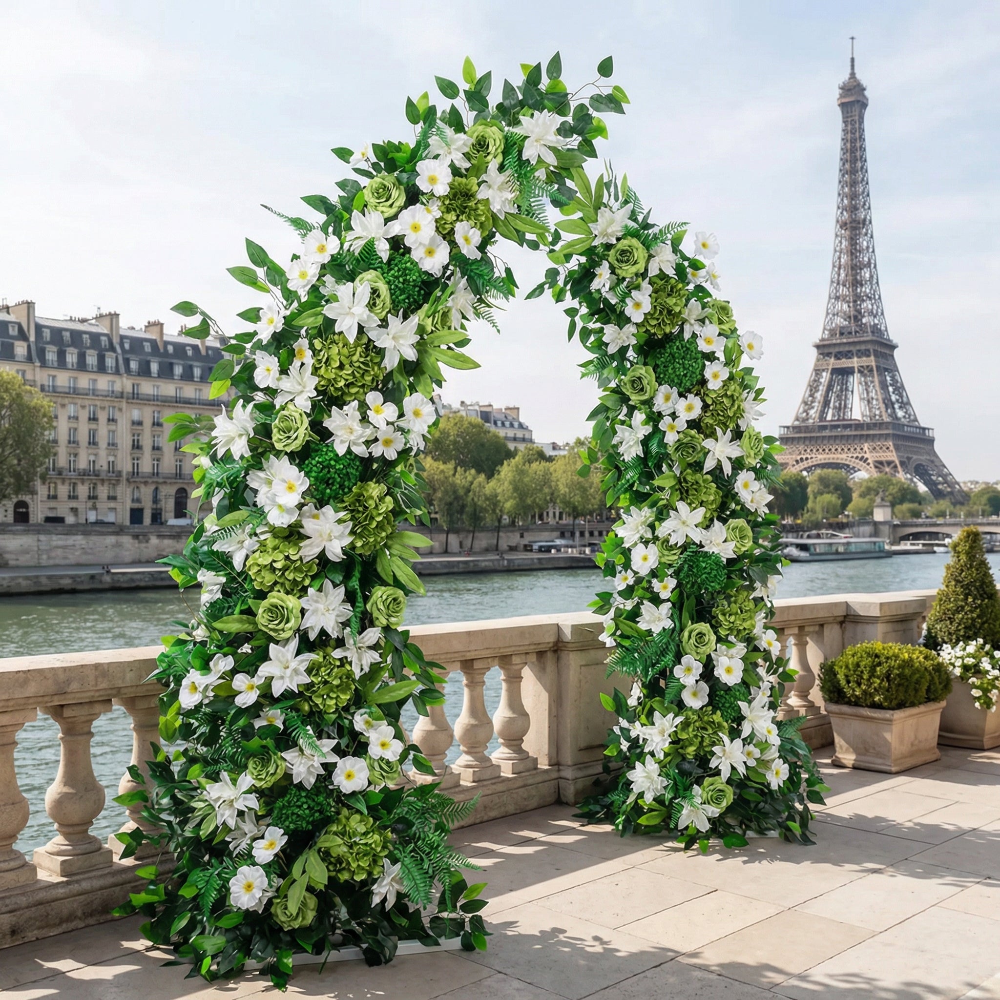 A timeless, symmetrical floral arch from Valar Flowers, crafted with a fresh palette of pure white lilies, roses, and vibrant green hydrangeas, intertwined with lush eucalyptus and fern foliage. Set on a sunlit Parisian riverside terrace with the iconic Eiffel Tower in the background, it creates a serene, elegant, and ethereal atmosphere perfect for luxury weddings and refined photoshoots.