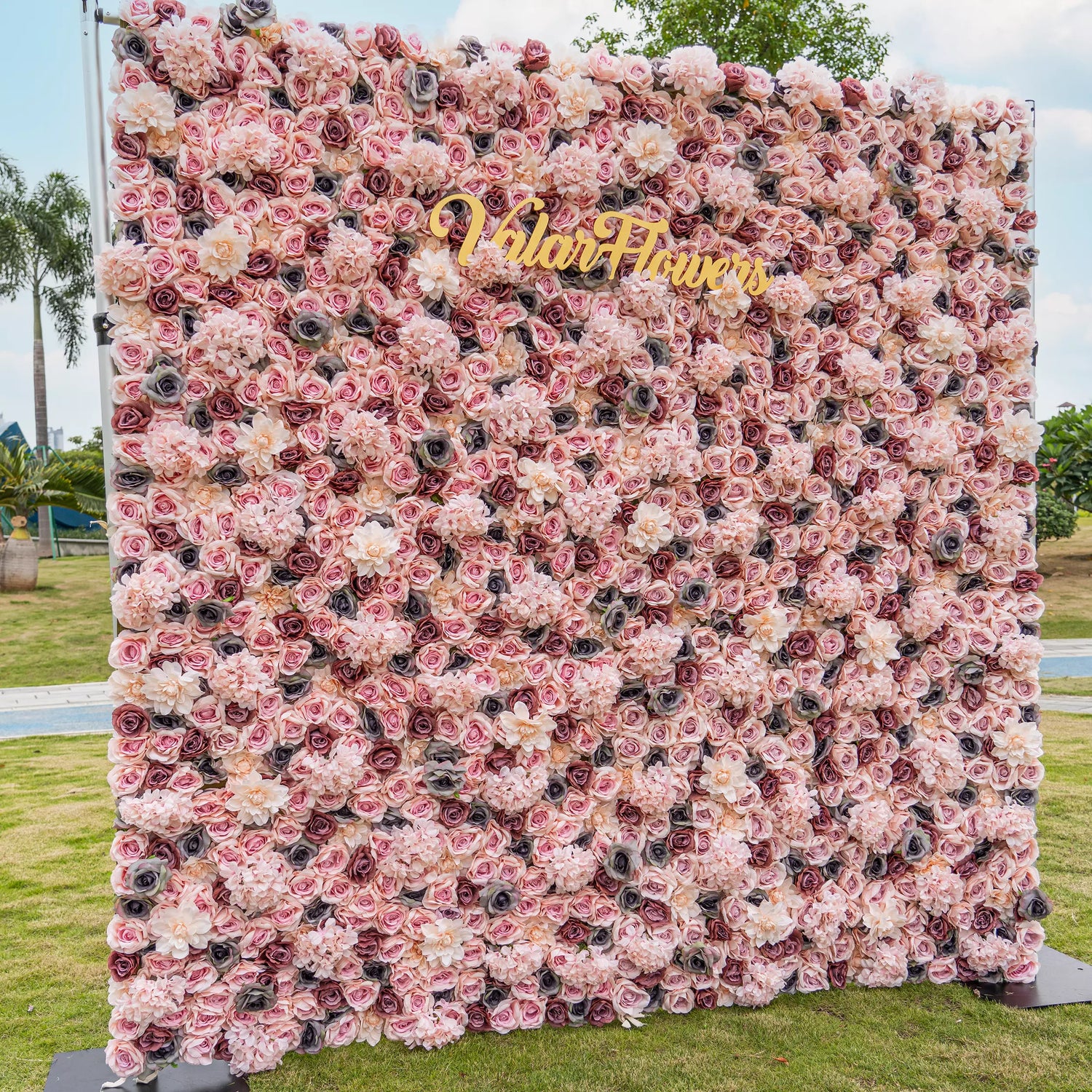 Blush Blossom Tapestry: An exquisite floral backdrop brimming with layers of soft pink and creamy white roses. Amidst the gentle petals, the golden "VlairFlowers" inscription gleams, set against a scenic city park. An embodiment of romance and elegance in nature&