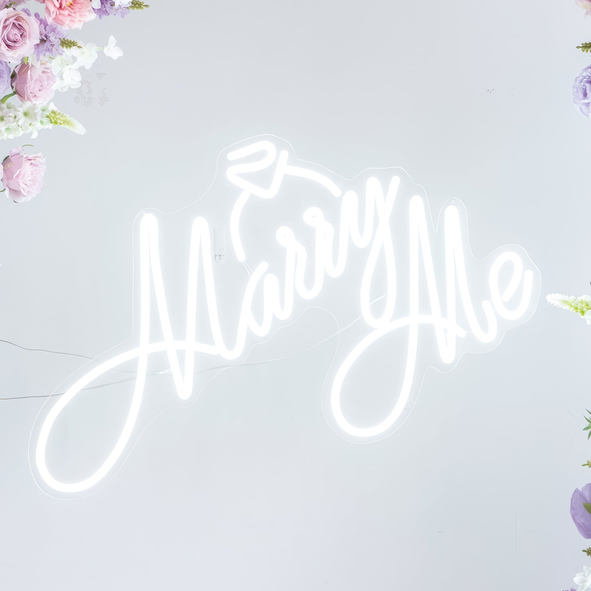 This bright white neon sign from Valar Flowers displays the romantic phrase "Marry Me" in a flowing, cursive script, topped with a delicate ring icon. Framed by soft pastel blooms, it creates a dreamy, intimate atmosphere ideal for proposals, engagement shoots, or romantic celebrations.