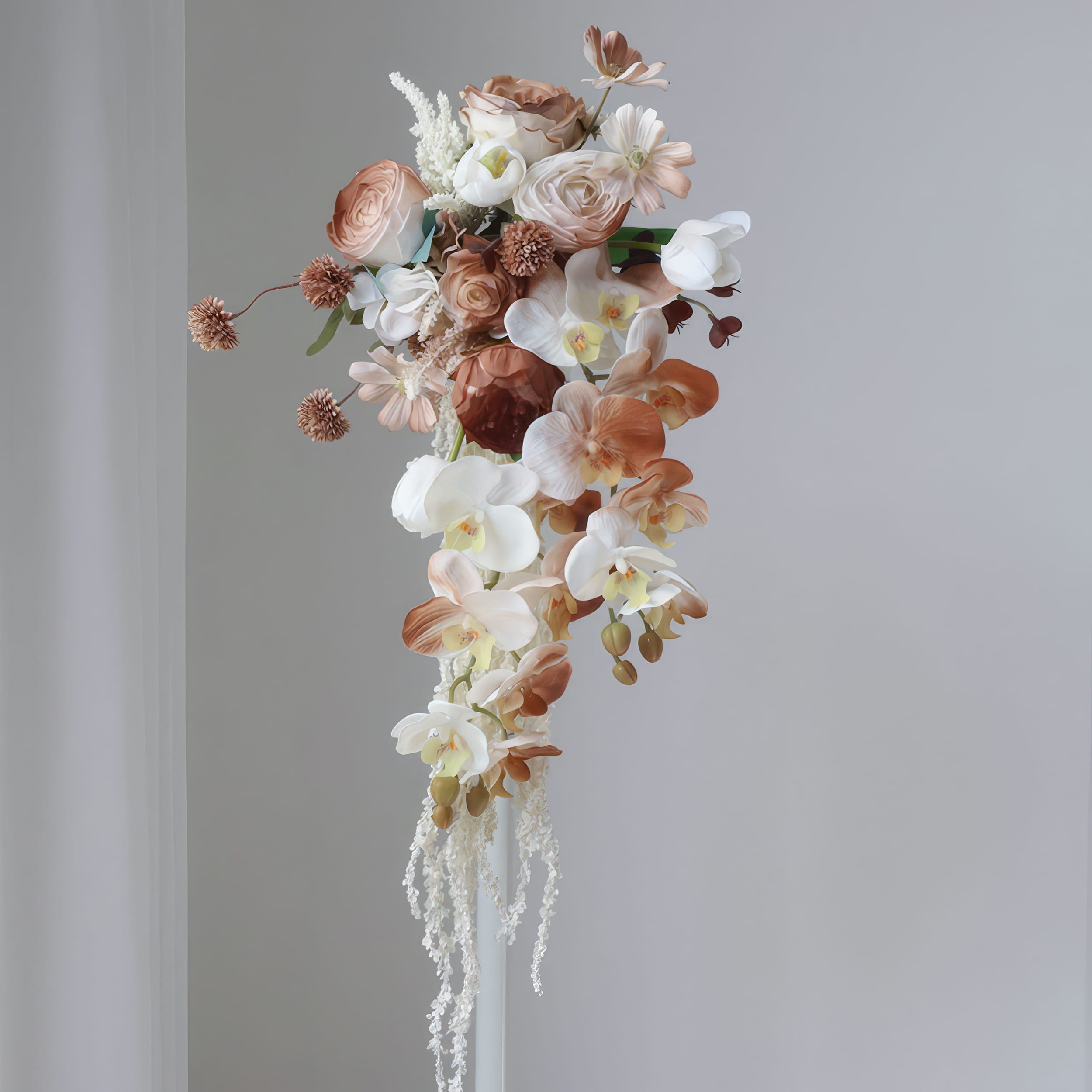 This is a cascading floral bouquet featuring a mix of blooms. It includes white and beige orchids, roses, and delicate filler flowers, with earthy - toned spherical blossoms. The flowing design and neutral color palette create an elegant, romantic look, perfect for weddings or special events.