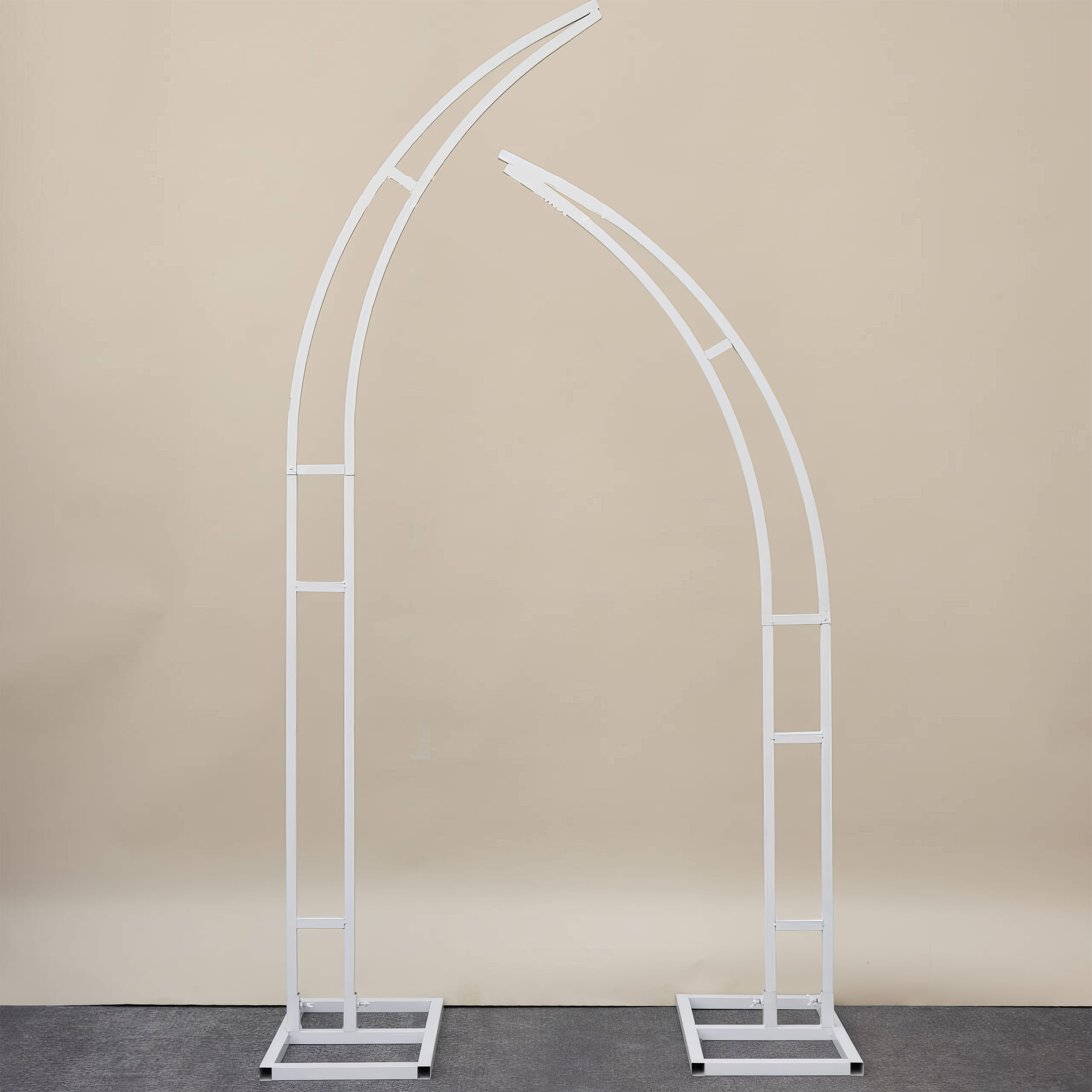 A sleek, white metal floral arch frame with a modern asymmetrical crescent design, featuring two curved support poles on square bases. The minimalist open-frame structure stands against a neutral beige backdrop, perfect for weddings, photoshoots, and event decor.