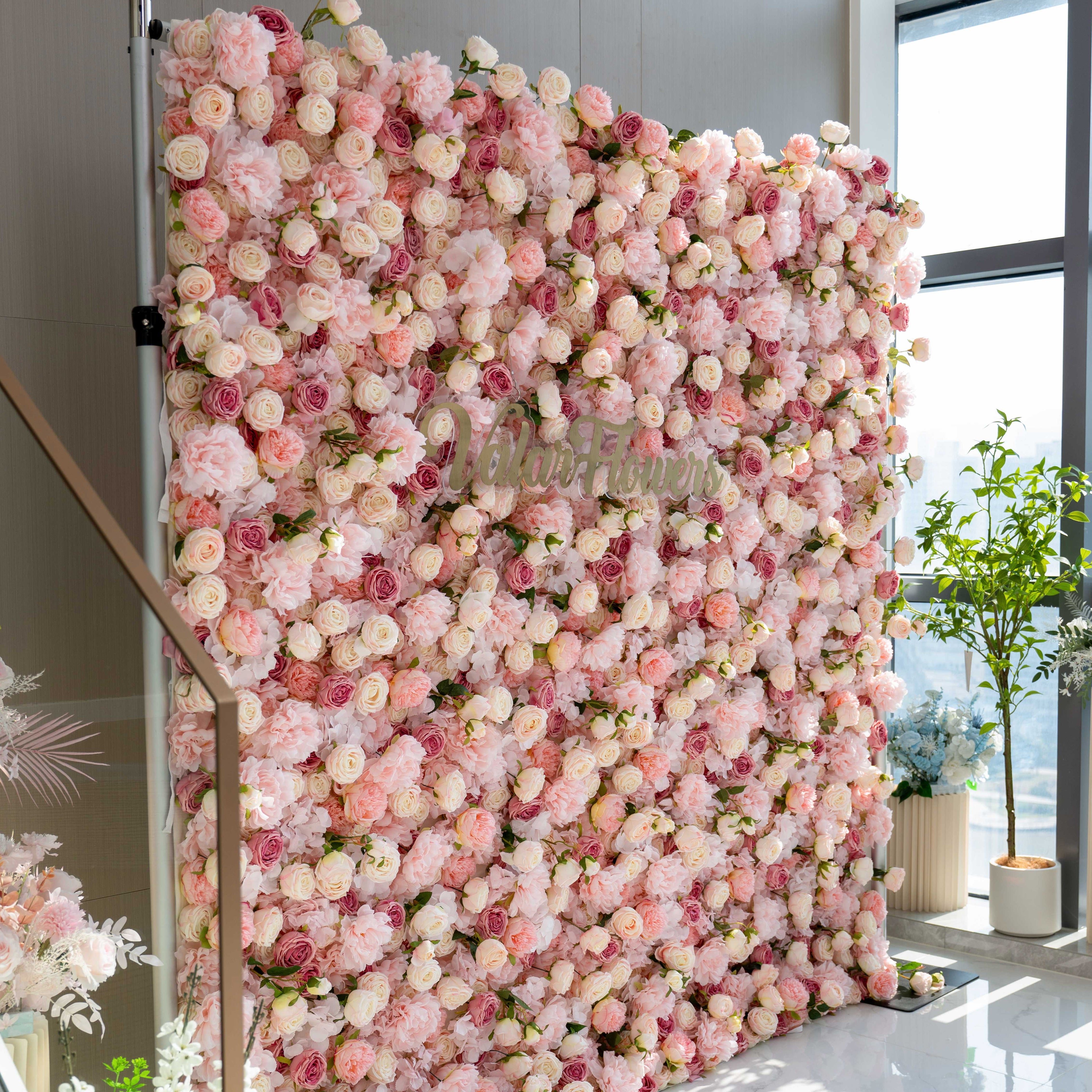 A large, square flower wall filled with pink and white roses and peonies. It has the text "Valar Flowers" on it. Surrounding plants add to the floral ambiance.