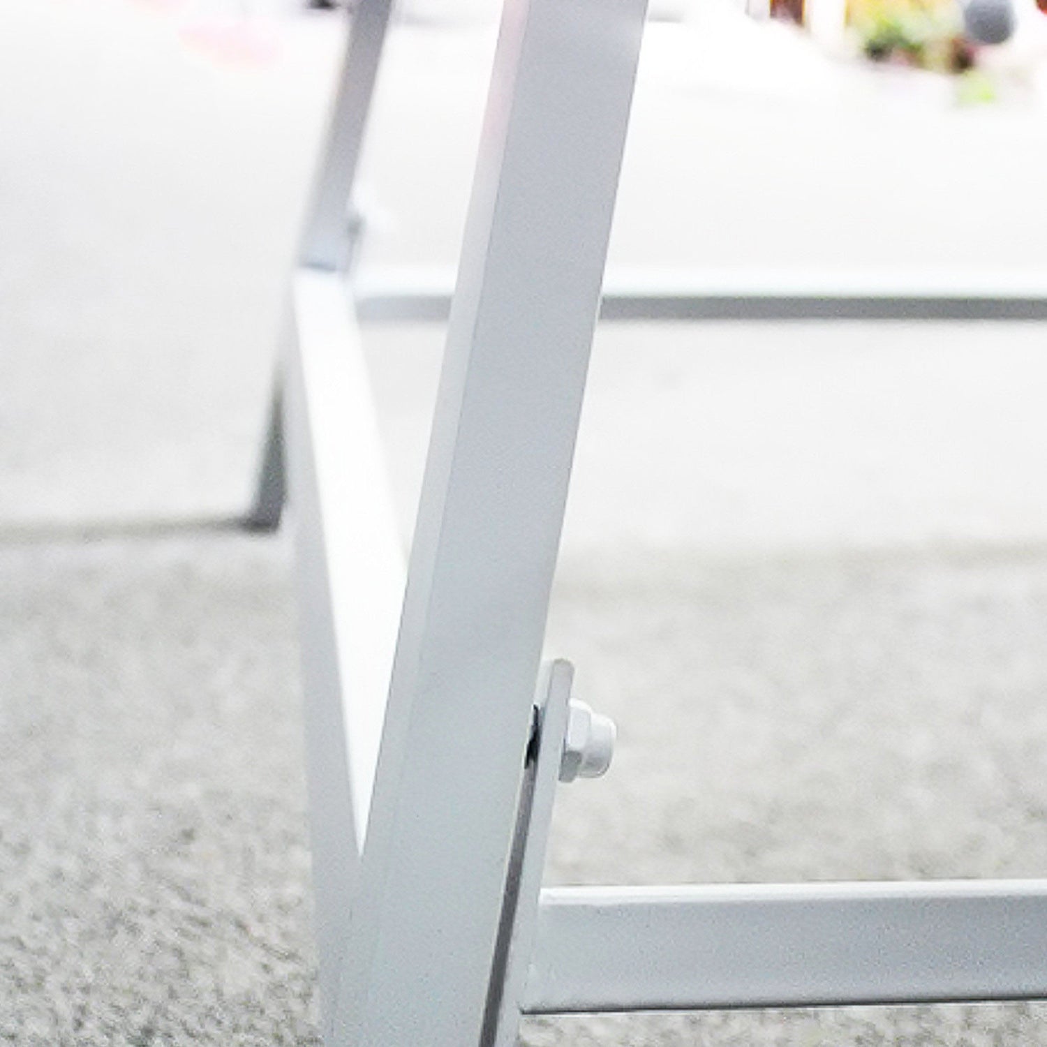 Close - up of a white metal frame joint, likely part of a decorative structure like a Ferris wheel stand. A bolt secures the triangular frame, showcasing simple yet sturdy construction. The background is blurred, emphasizing the metalwork detail.