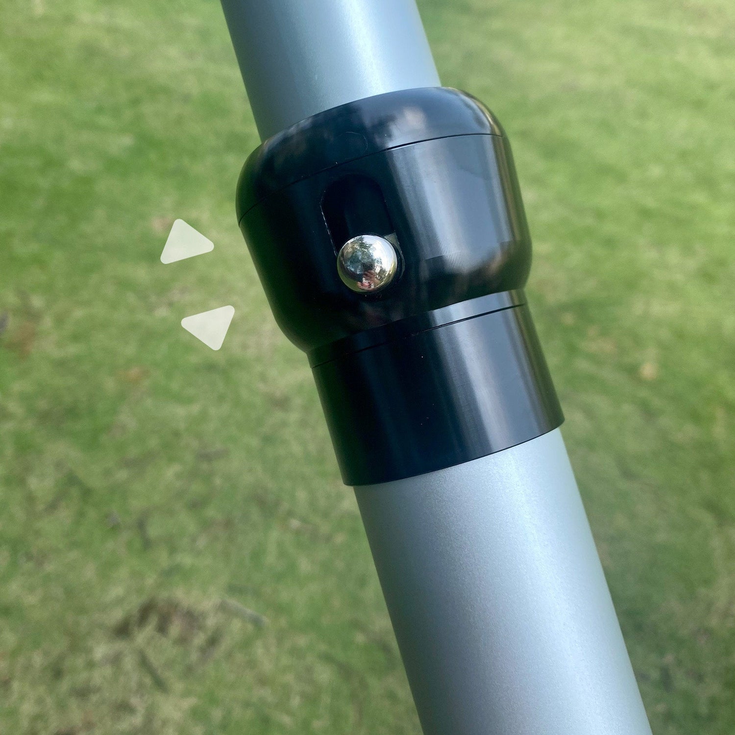 The image shows a close - up of a black connector on a silver metal pole, likely part of a bar system. A metallic knob is visible on the connector, and two white arrow - like shapes point to it, set against a grassy background.