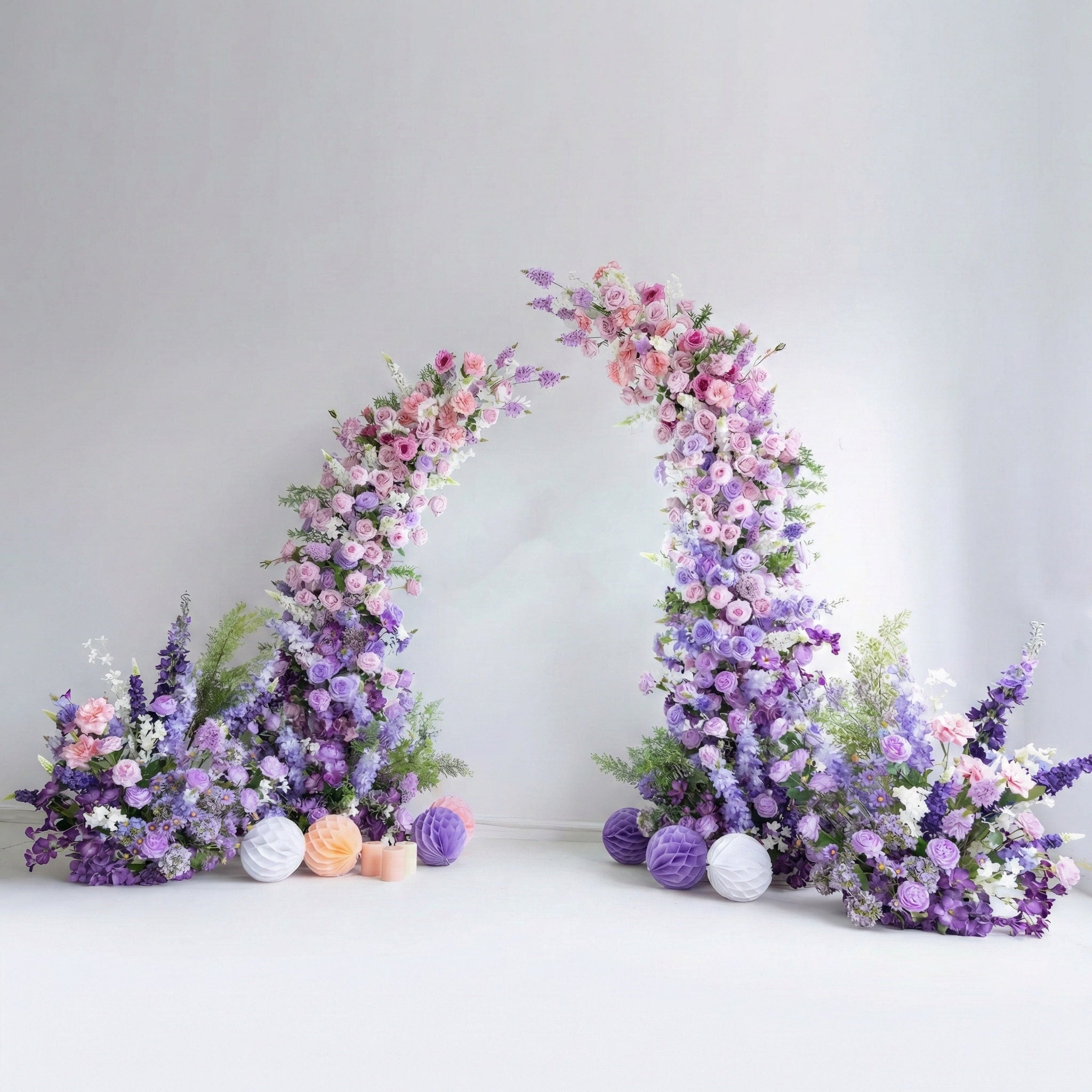 This elegant floral arch from Valar Flowers features a soft pastel palette of blush pink, lavender, and white blooms—including roses, hydrangeas, and delphiniums—arranged in two tall, cascading columns. Set against a minimalist white backdrop, the design evokes a romantic, sophisticated atmosphere ideal for weddings, engagement photoshoots, or elegant celebrations.