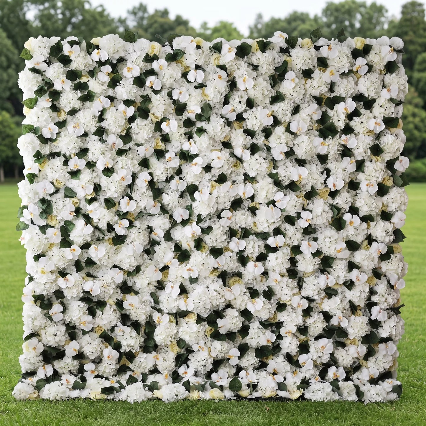 Premium full-panel white artificial flower wall covered in dense hydrangeas, orchid blooms, cream roses and lush green foliage, set on a sunlit outdoor lawn. Zero-upkeep, reusable floral backdrop with soft all-white tones ideal for wedding ceremonies, bridal photo booths, baby showers, boutique displays and minimalist event decor, creating elegant, clean, Instagram-perfect neutral backdrops.