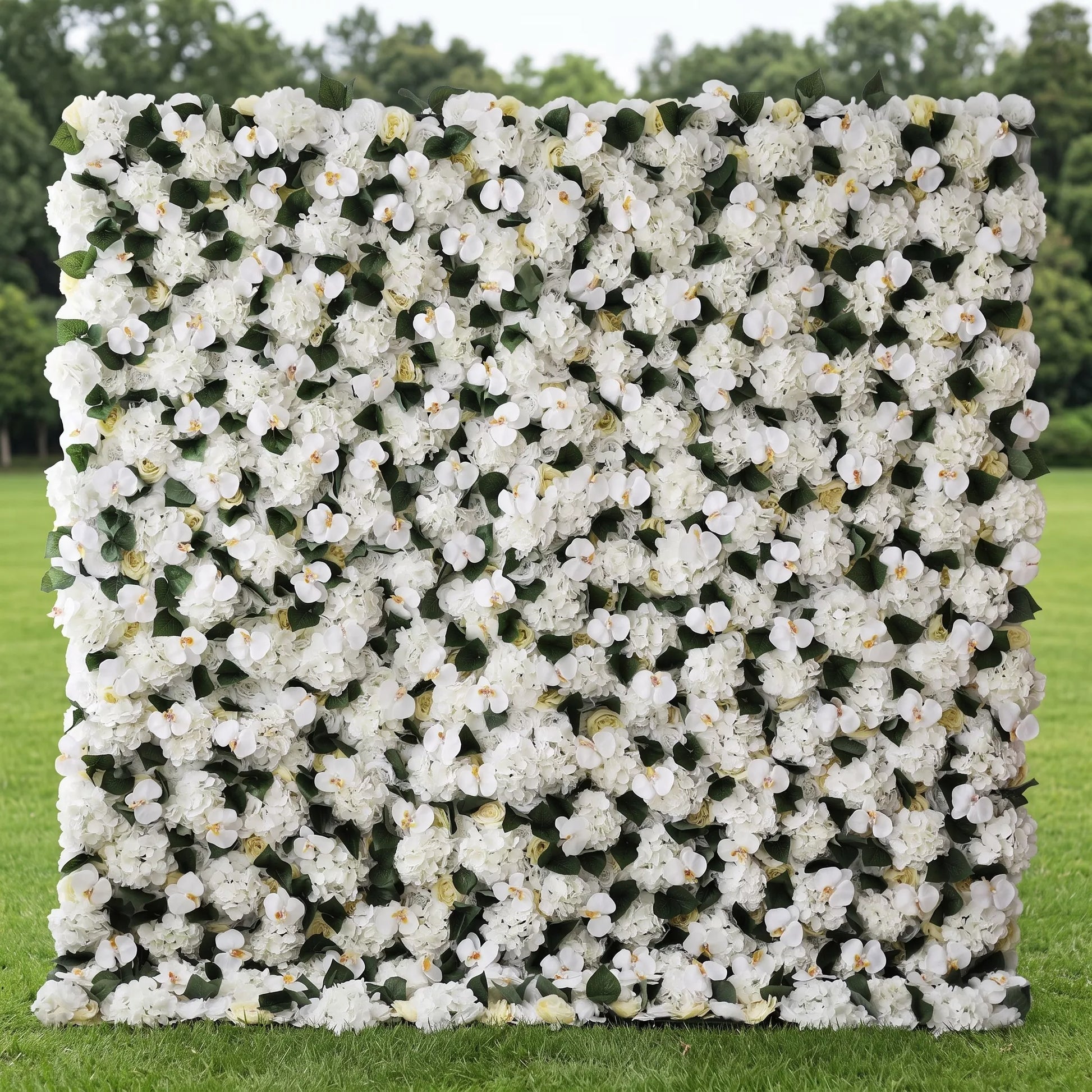 Premium full-panel white artificial flower wall covered in dense hydrangeas, orchid blooms, cream roses and lush green foliage, set on a sunlit outdoor lawn. Zero-upkeep, reusable floral backdrop with soft all-white tones ideal for wedding ceremonies, bridal photo booths, baby showers, boutique displays and minimalist event decor, creating elegant, clean, Instagram-perfect neutral backdrops.
