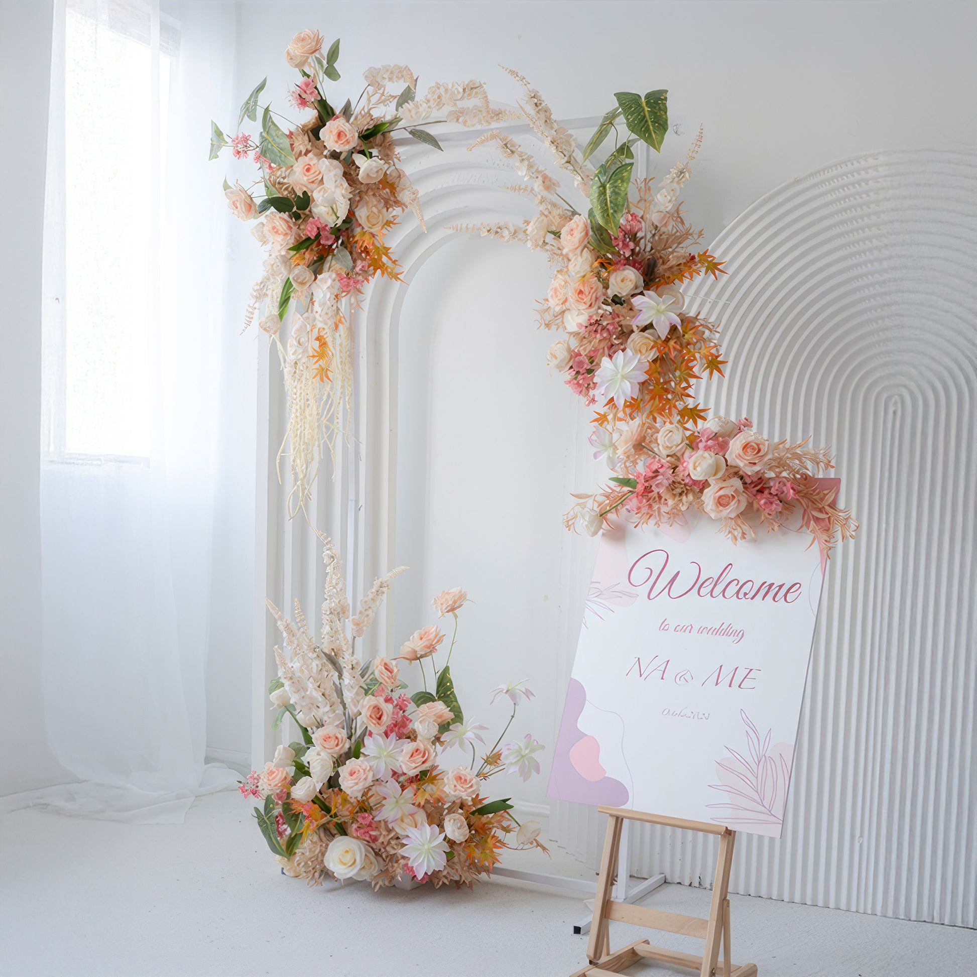 The image shows a wedding - like setup with an arch adorned with artificial roses, daisies, and other blooms in soft pinks, peaches, and whites. A "Welcome" sign adds to the inviting, romantic style. 