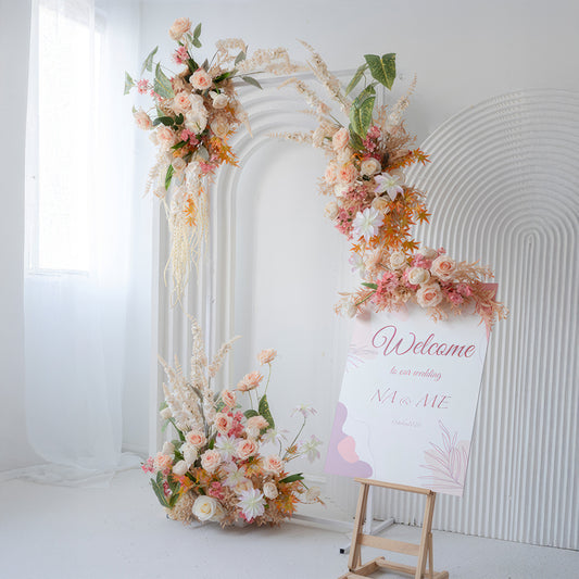 The image shows a wedding - like setup with an arch adorned with artificial roses, daisies, and other blooms in soft pinks, peaches, and whites. A "Welcome" sign adds to the inviting, romantic style. 