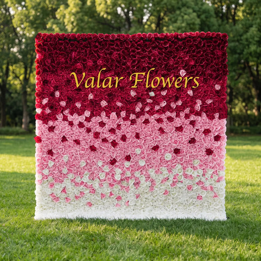 Stunning ombre artificial rose flower wall with gradient burgundy, blush pink and creamy white blooms, set on a sunlit green lawn. Centered golden "Valar Flowers" branding adds custom business display appeal. Reusable, low-maintenance floral backdrop ideal for wedding photo booths, boutique storefronts, brand events and social media shoots, delivering romantic layered texture and eye-catching gradient color styling.