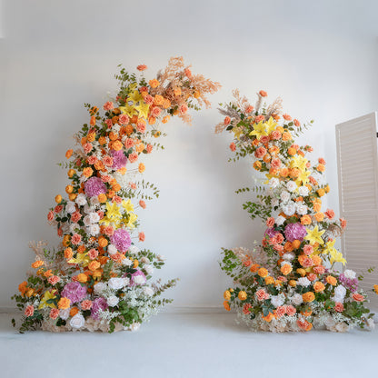 This floral arch is a vibrant display of colors, featuring a mix of orange, yellow, pink, and white flowers. There are roses, hydrangeas, lilies, and other blooms, complemented by green foliage and some dried elements. It creates a lively and eye - catching look, perfect for adding a festive touch to weddings, parties, or other special events. 