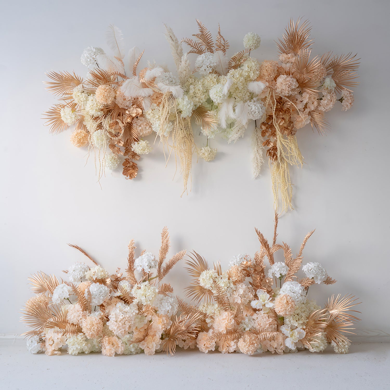 The image shows artificial floral decor with hydrangea - like flowers, palm fronds, and feathers. Colors are white, peach, and gold - toned, creating a luxurious, modern style perfect for event backdrops. 