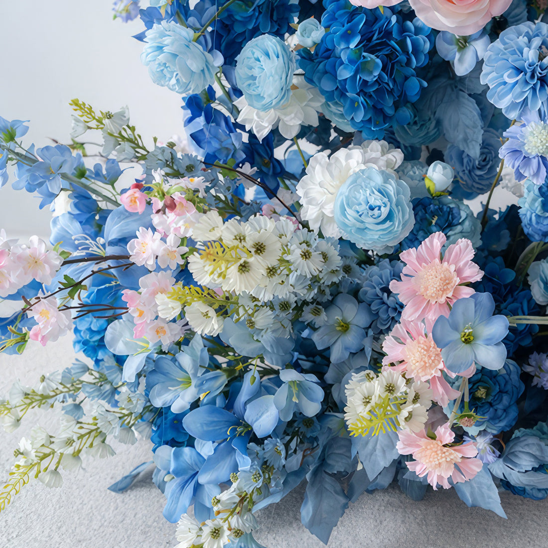 This floral ensemble showcases a delightful mix of blues, whites, and soft pinks. With hydrangeas, roses, and smaller blooms, it exudes a sweet and romantic style. Perfect for weddings, events, or adding a touch of charm to any space.