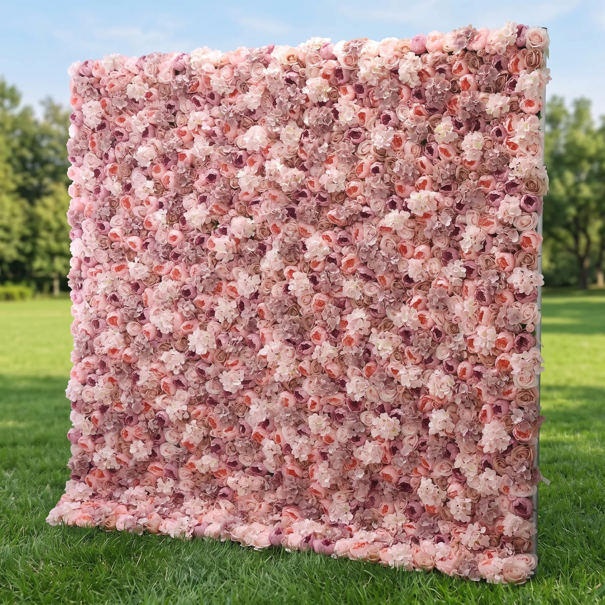 Lush full-panel blush artificial flower wall densely packed with layered dusty pink, peach, mauve and cream roses mixed with delicate filler blooms, displayed outdoors on a vibrant green lawn. This reusable, maintenance-free floral backdrop delivers soft romantic texture, ideal for wedding photo booths, bridal showers, boutique retail displays and pastel-themed social media content shoots for elegant, eye-catching event styling.